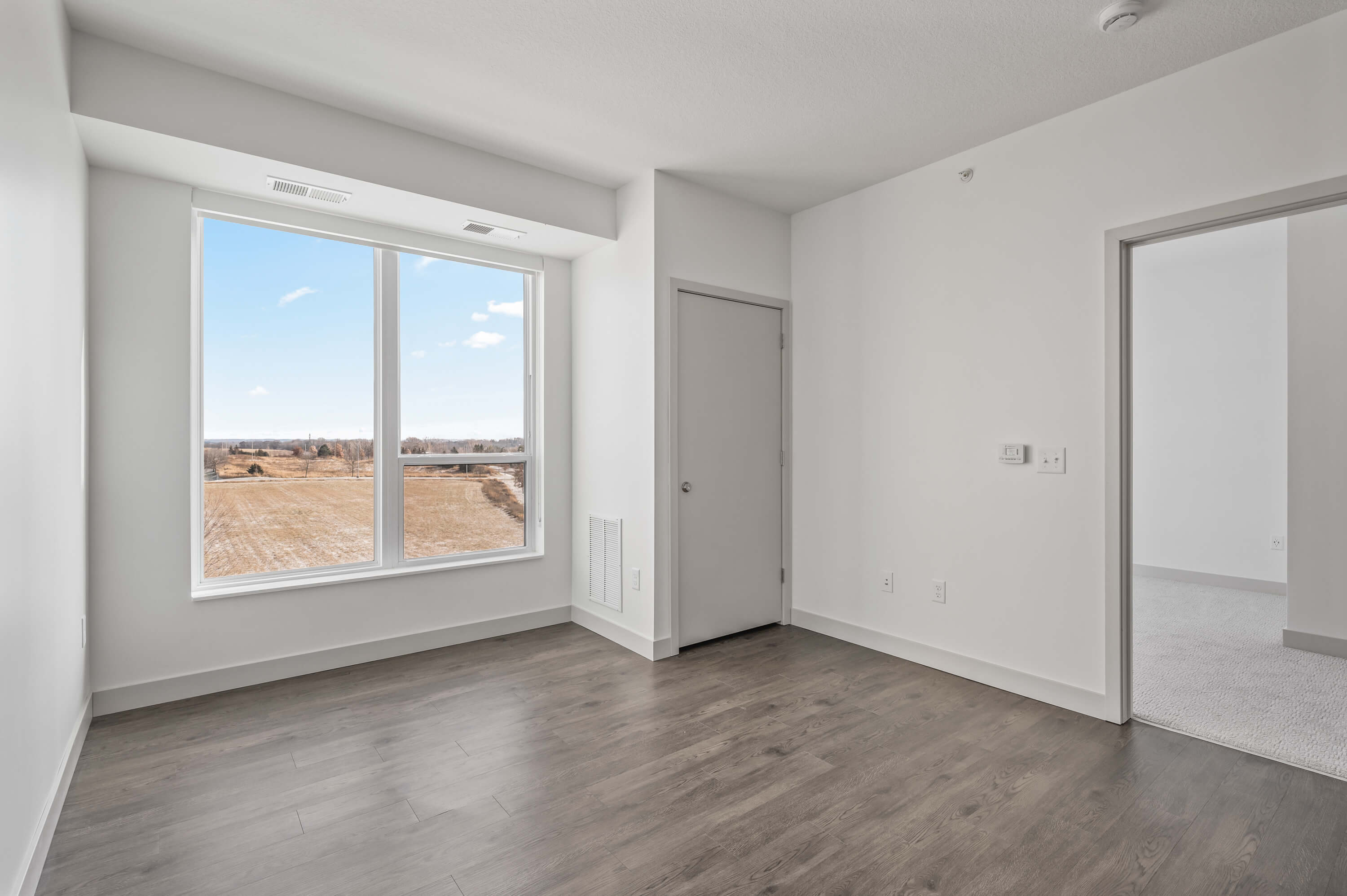 Room with a window offering a view of an open field, featuring hardwood flooring.