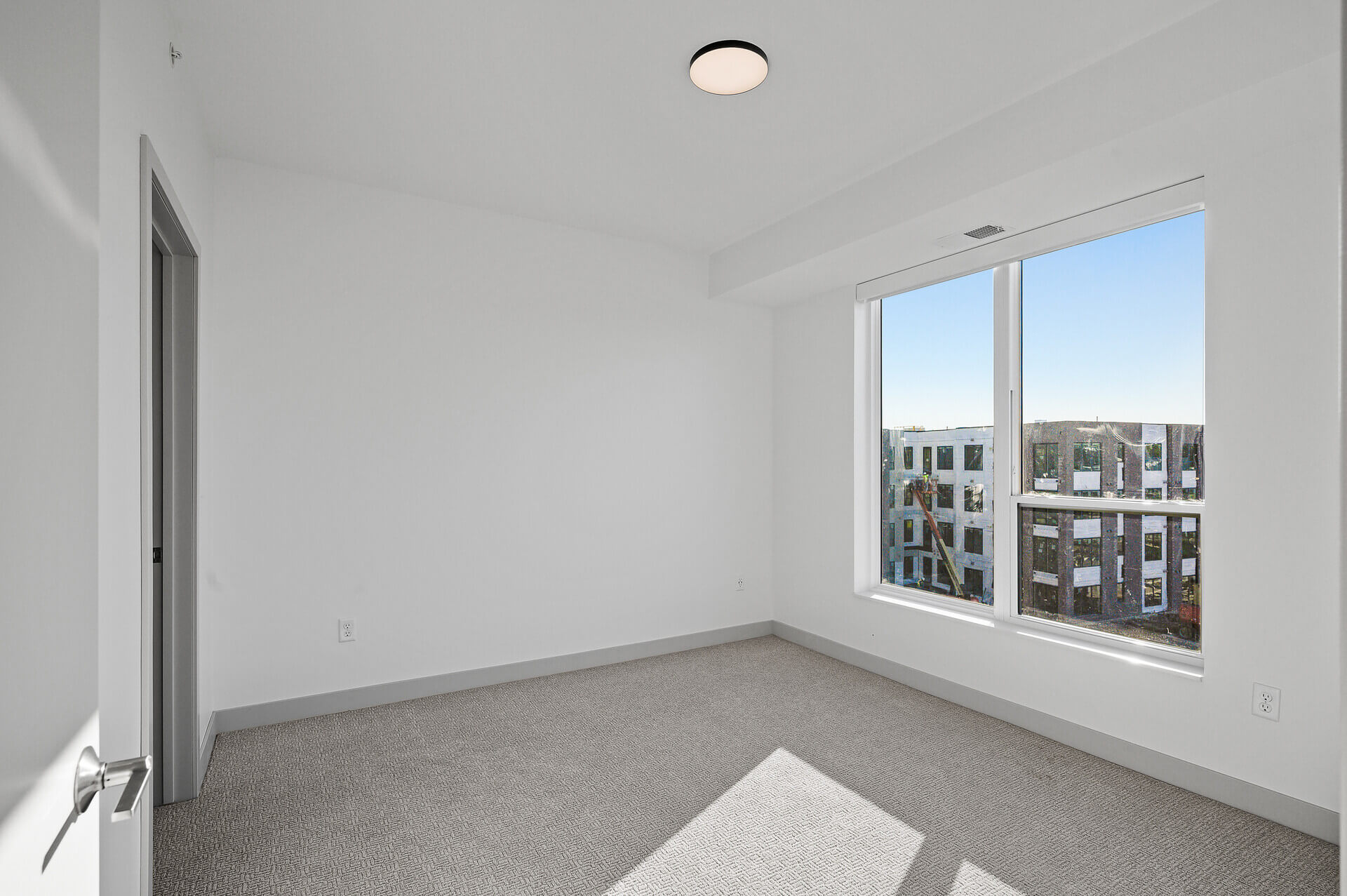 Carpeted bedroom with large window overlooking construction outside