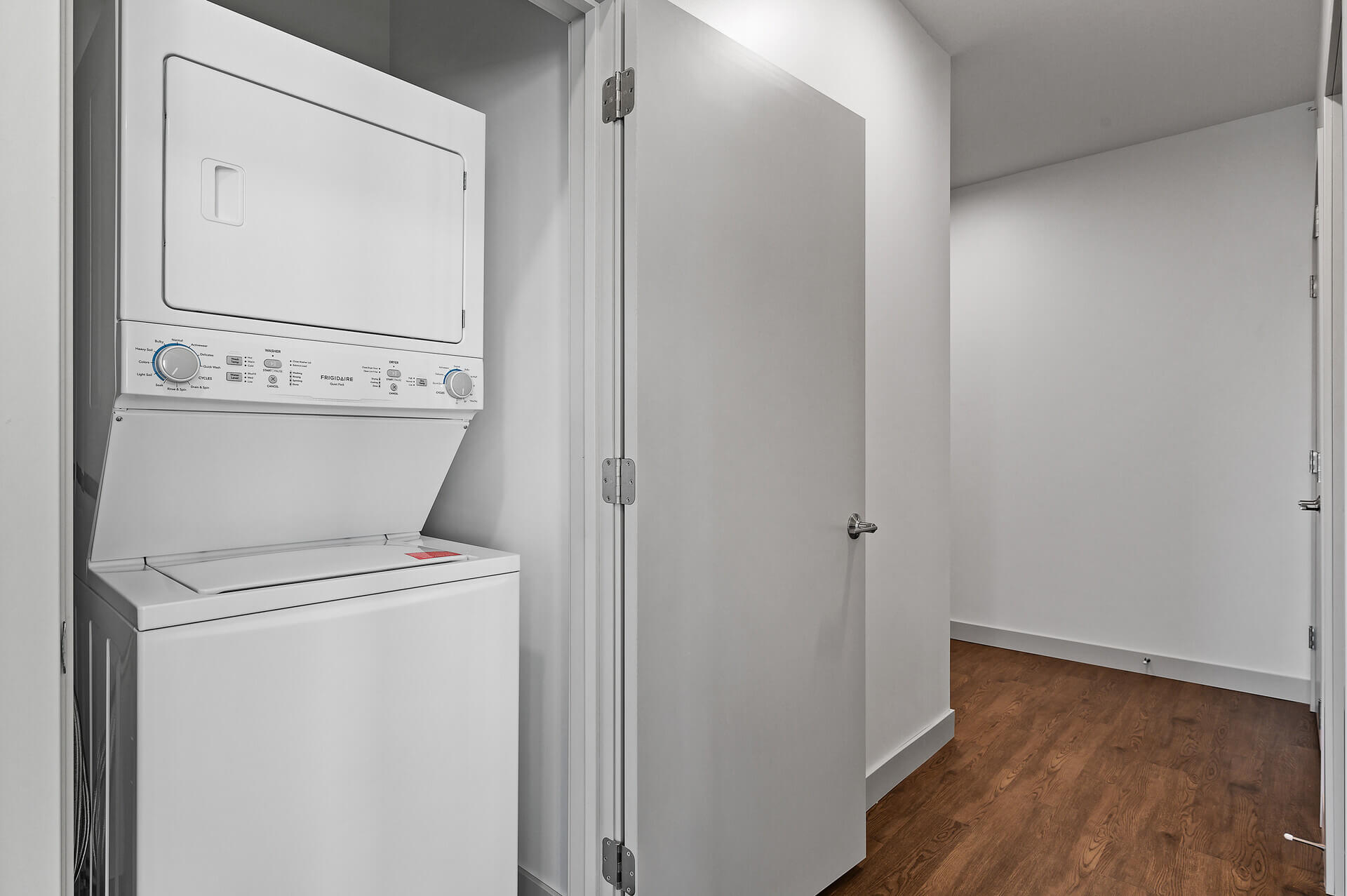 Stacked washer and dryer unit next to an open door leading into a hallway.