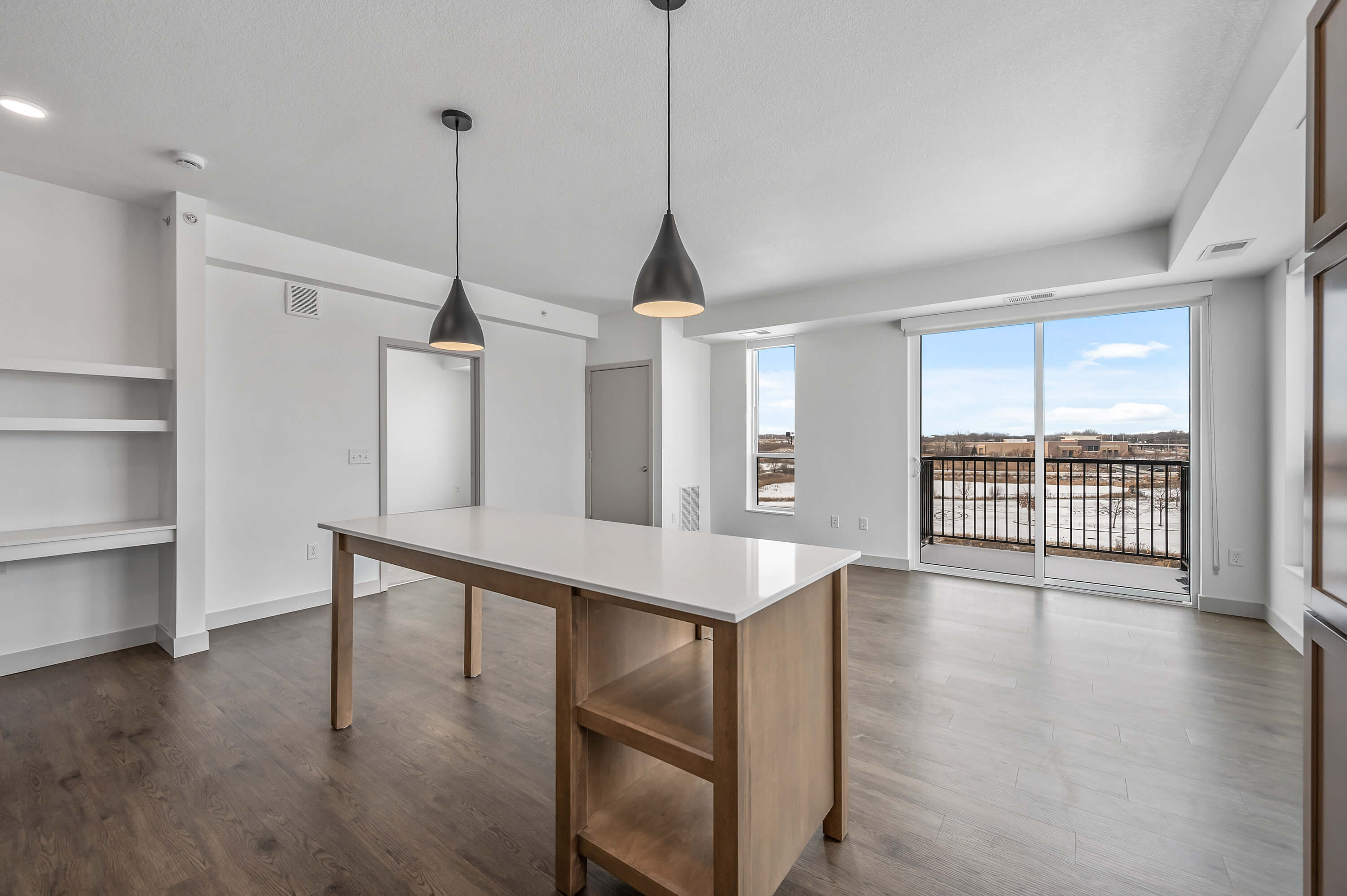 Another view of the living room and balcony with wood flooring and bright white walls.