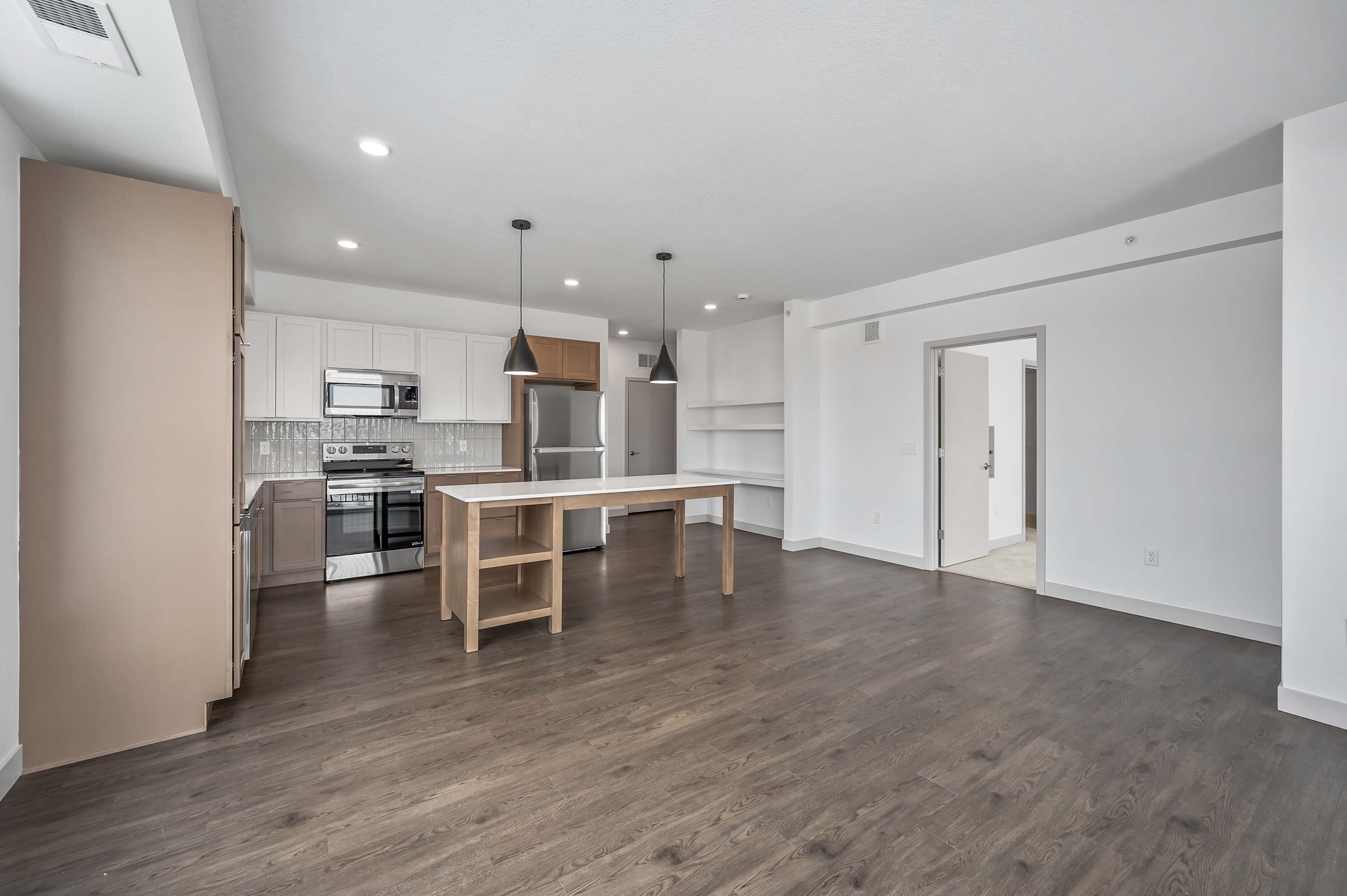 An open-concept kitchen and living area with pendant lights, white cabinetry, and dark wood flooring.