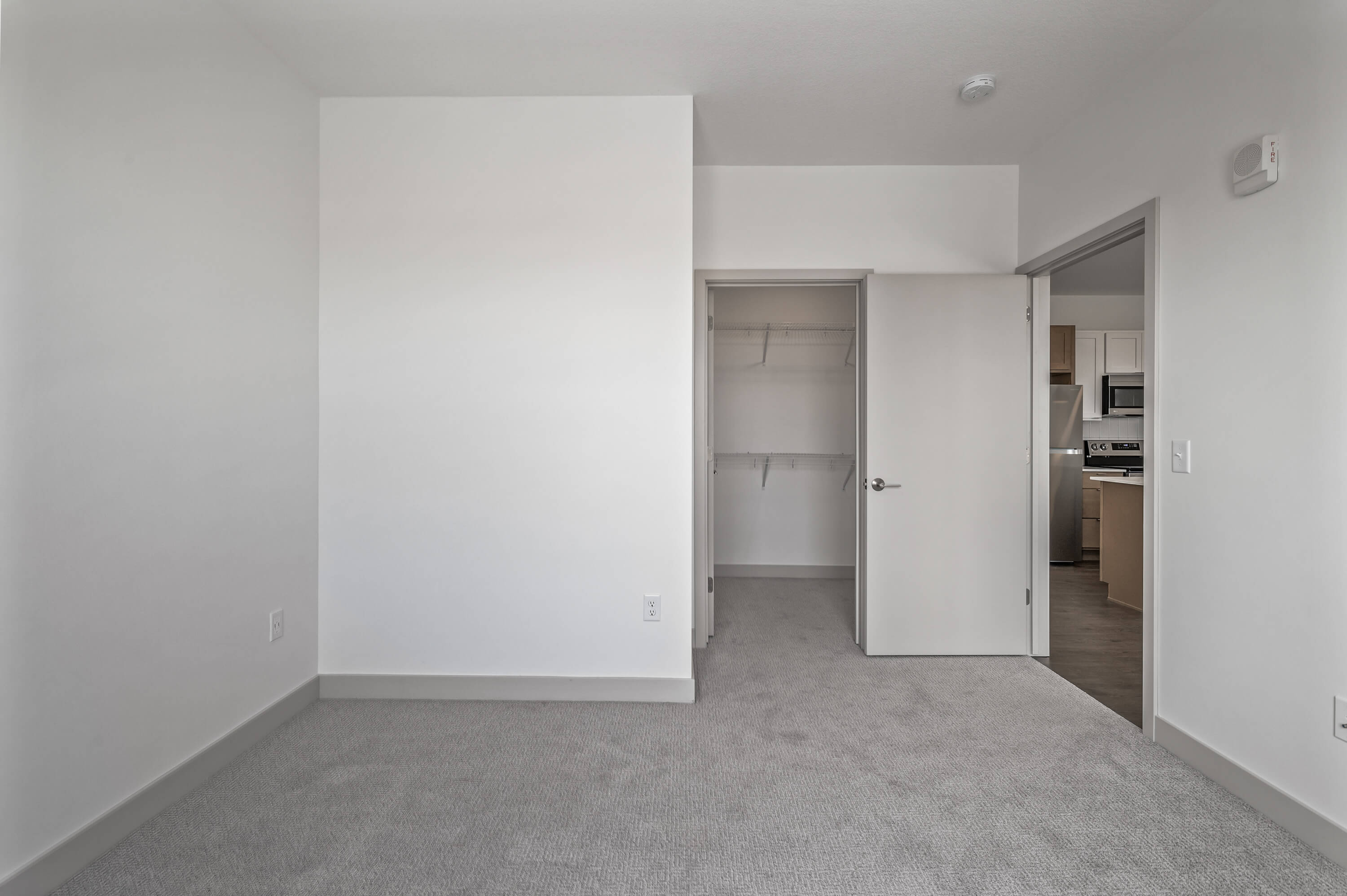 Bedroom featuring a closet with open doors, carpeted flooring, and an entryway leading to the kitchen.