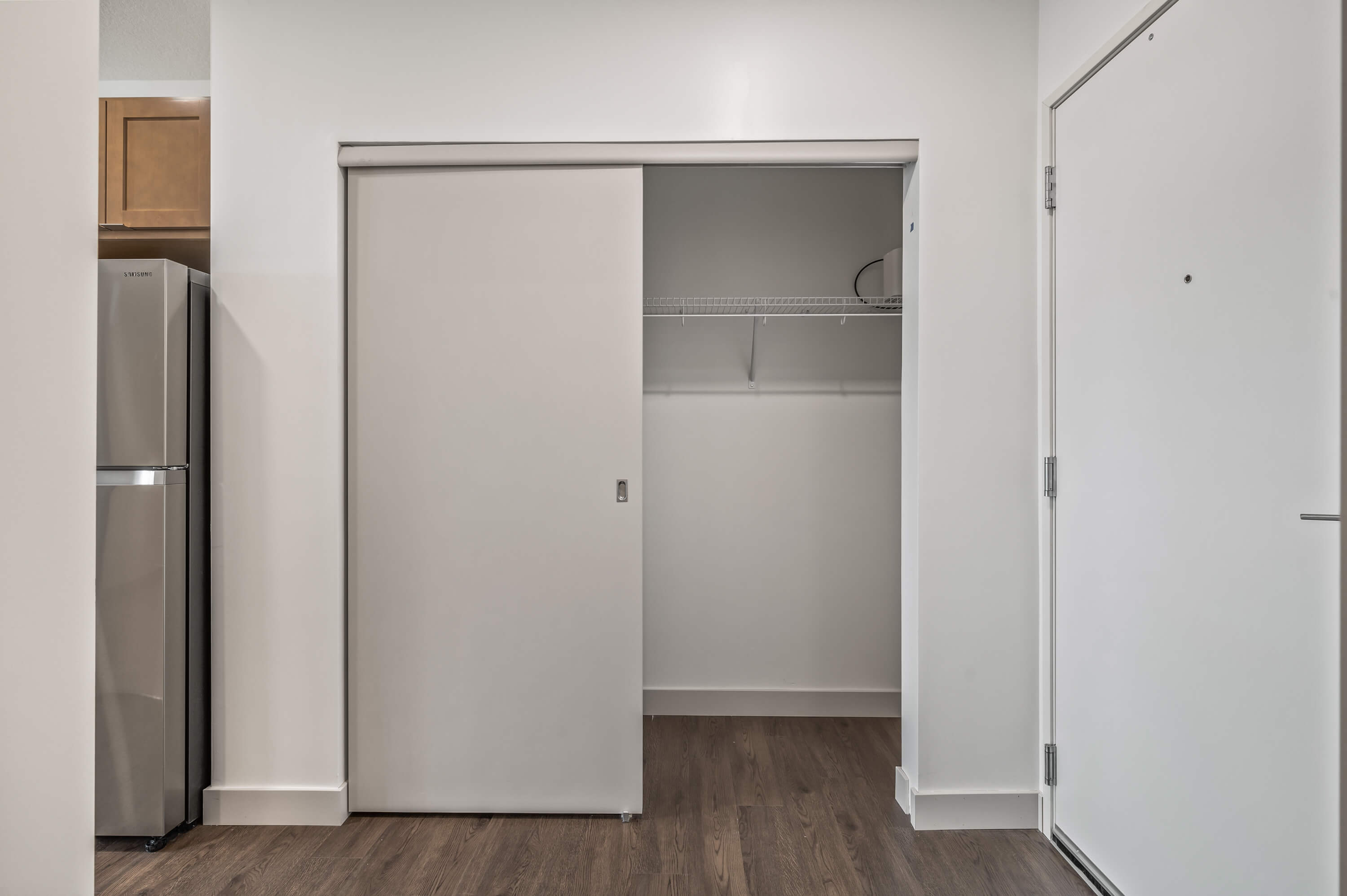 Entryway with a sliding door closet, stainless steel refrigerator visible in the adjacent kitchen.