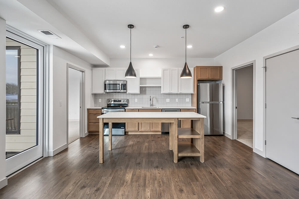 Modern apartment kitchen with mixed wood and white cabinetry, stainless steel appliances, and a center island