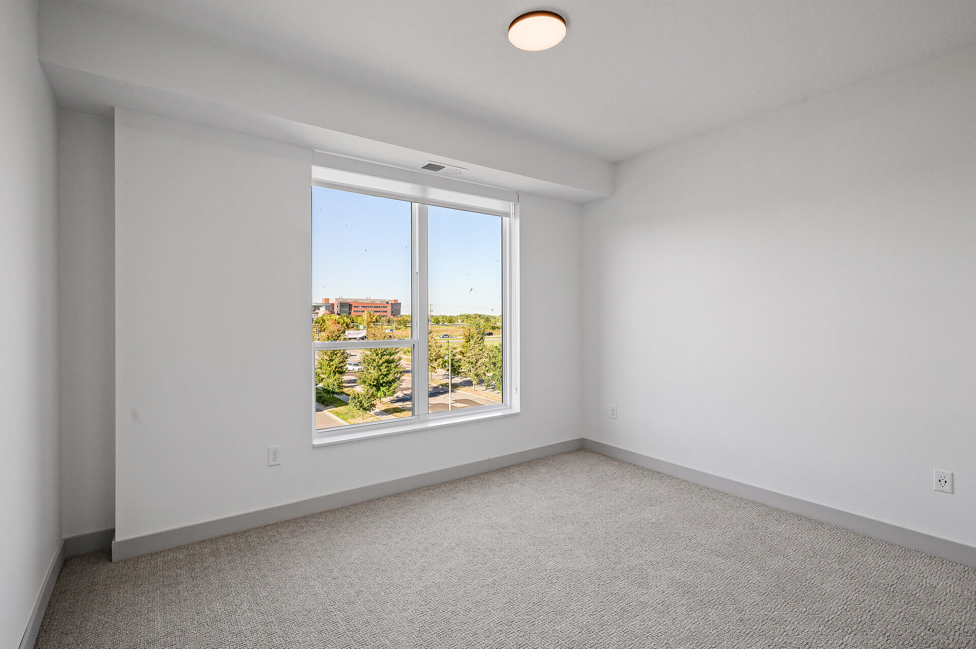 Bedroom with large window and a view of trees and buildings outside.