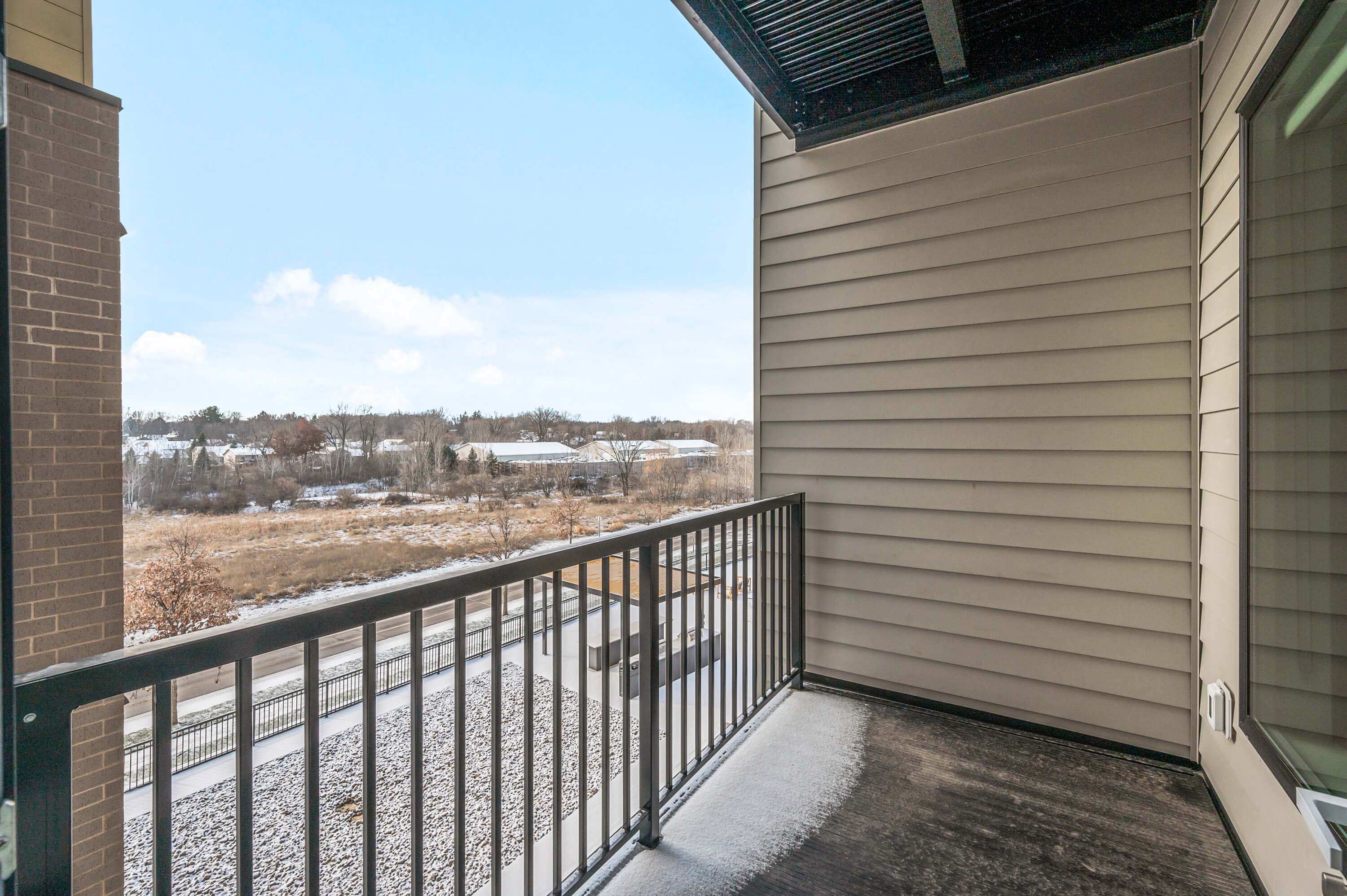 Balcony with a view of a snowy landscape, black metal railing, and tan siding.