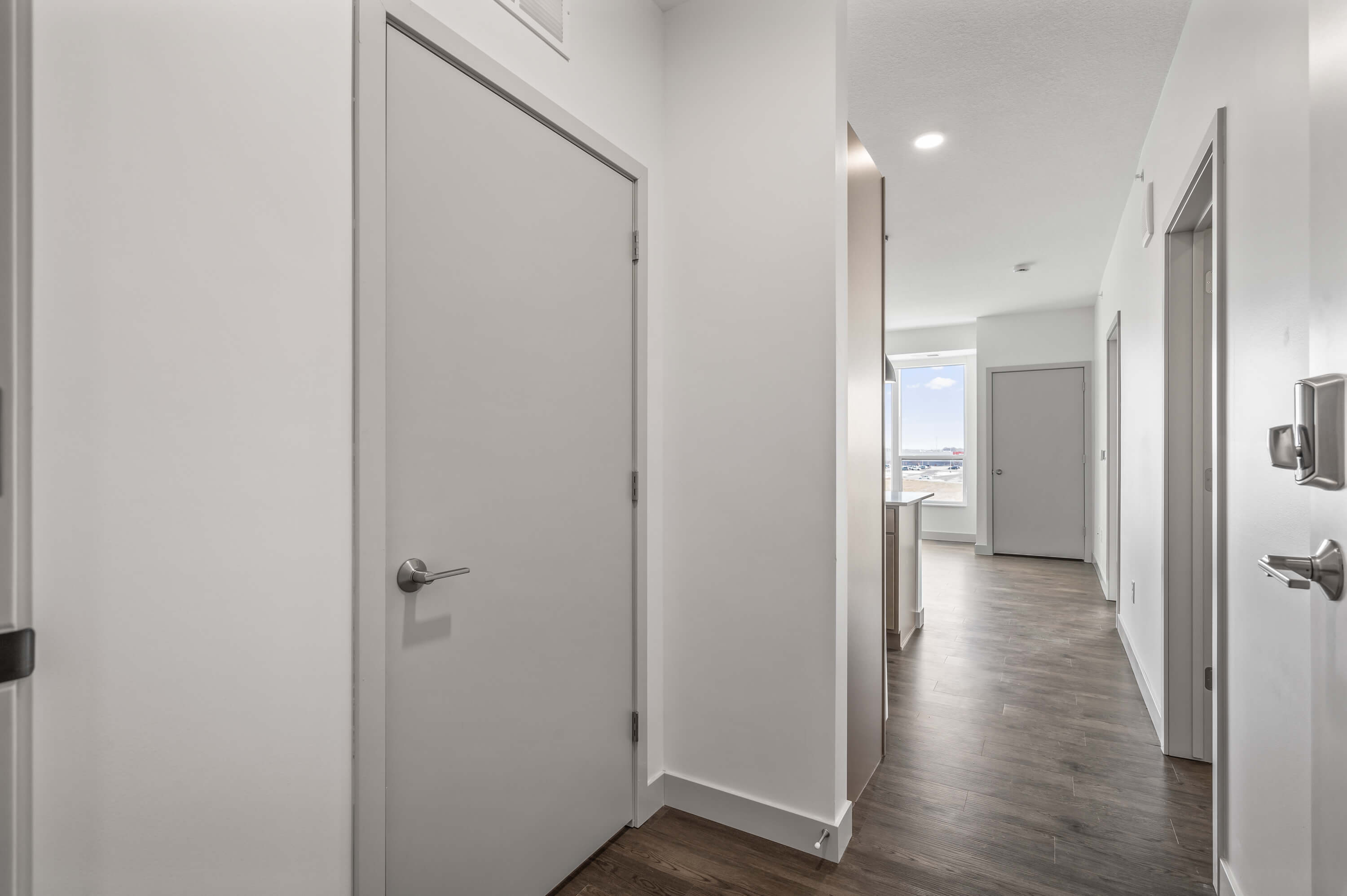 View of the hallway with doors leading to the kitchen and rooms, featuring hardwood floors.