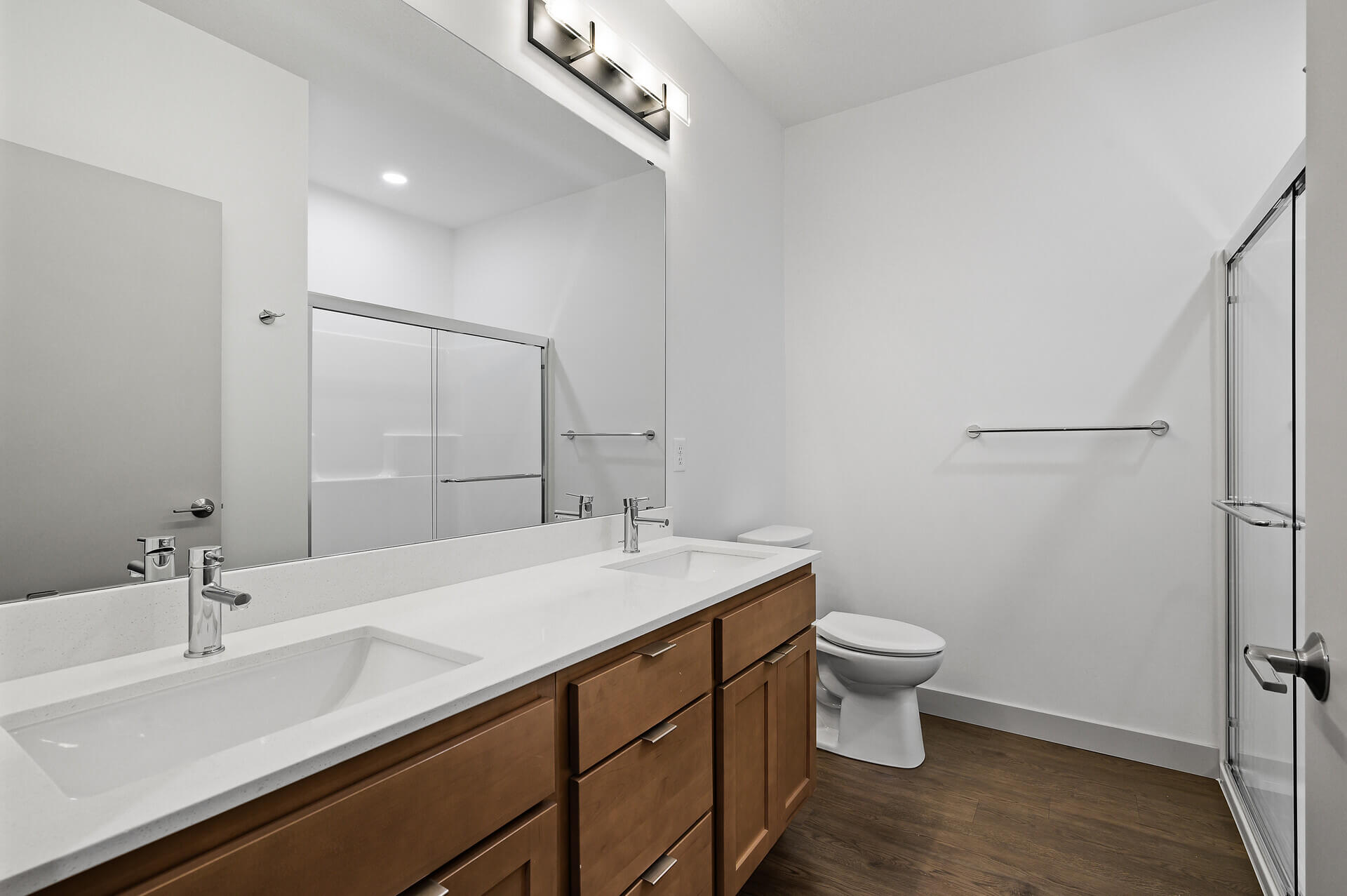 Modern bathroom with a double sink vanity, glass-enclosed shower, and wooden cabinets.