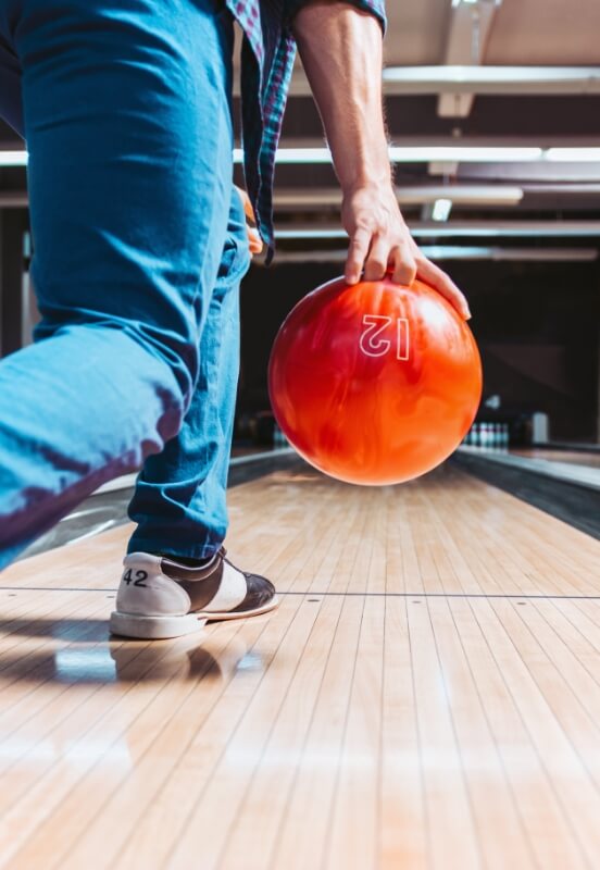 A bowler's hand holding a red bowling ball, ready to roll it down the alley, with focus on the shoes and the lane.