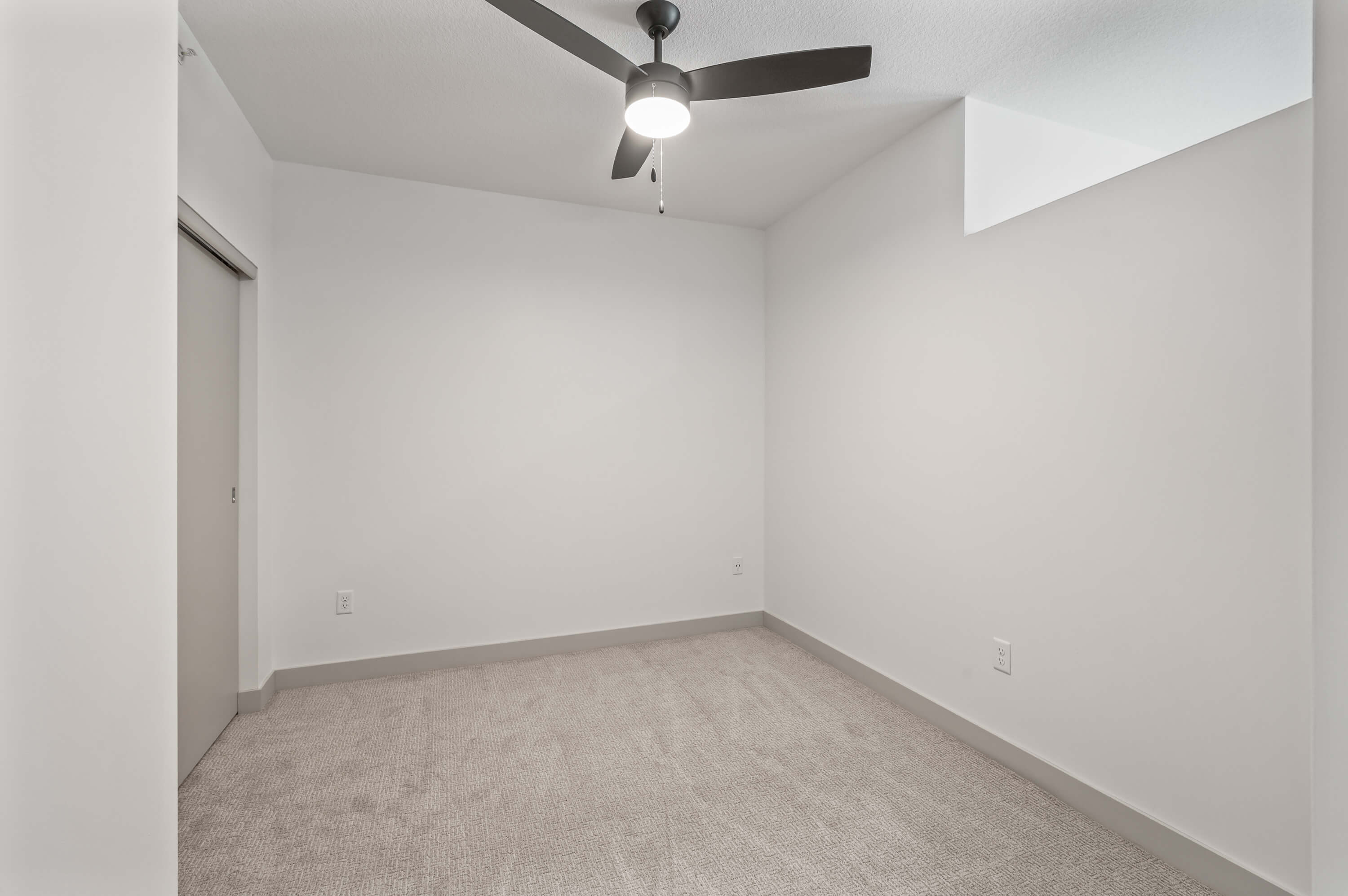 Bedroom with white walls, gray carpet, a ceiling fan, and a sliding closet door.