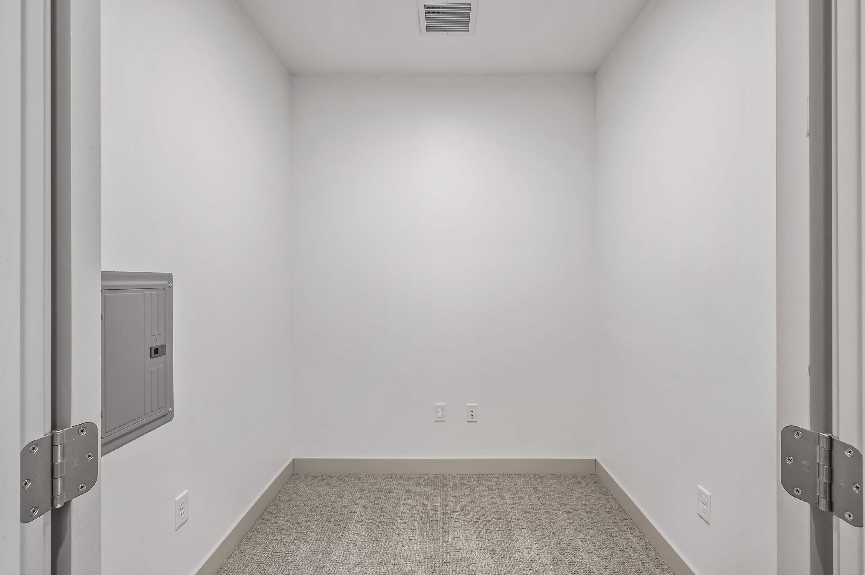 Small room with carpet flooring, white walls, and a utility panel.