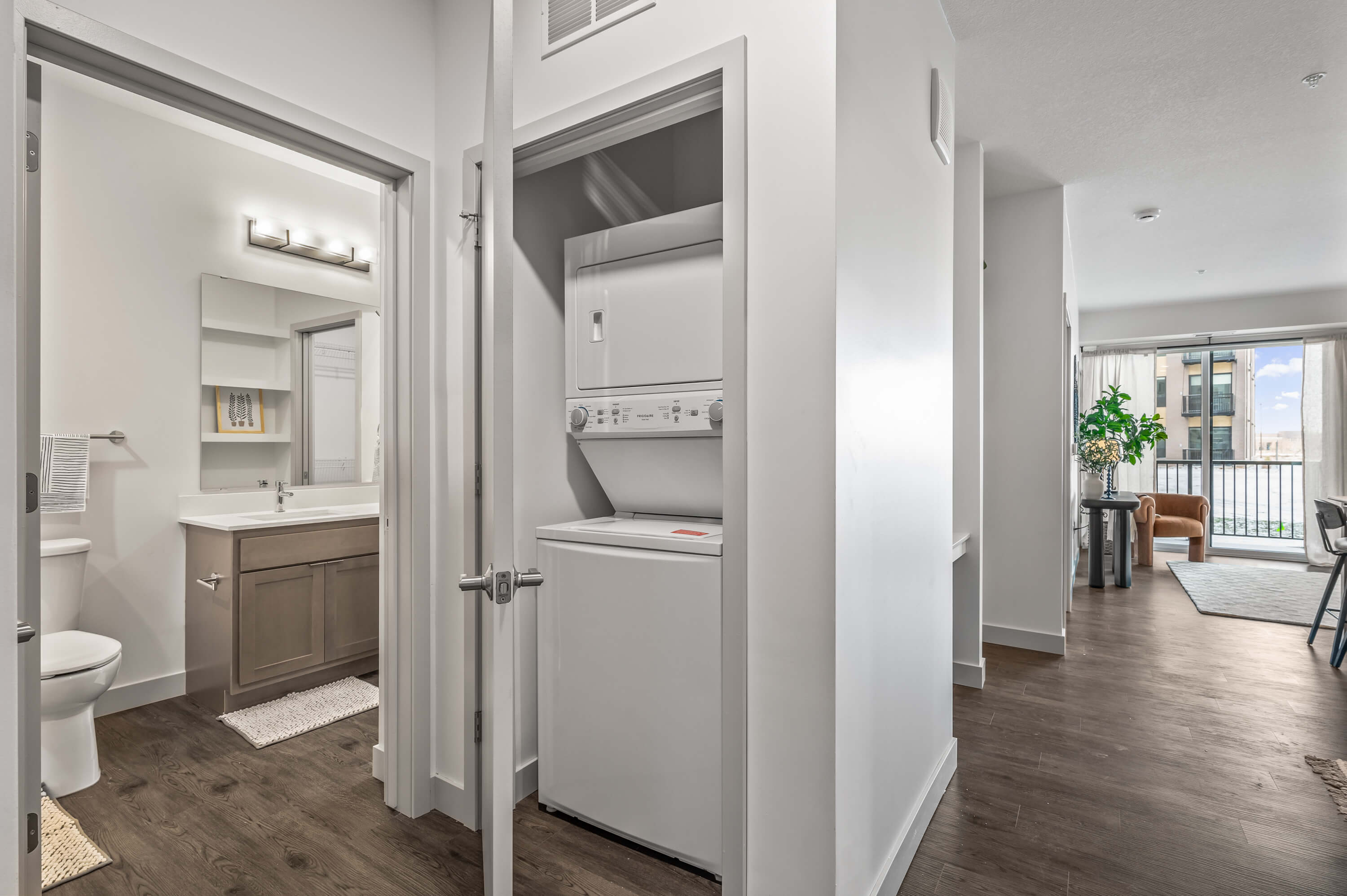 Hallway view featuring a bathroom and a compact laundry closet with a stacked washer and dryer, leading to a living area.