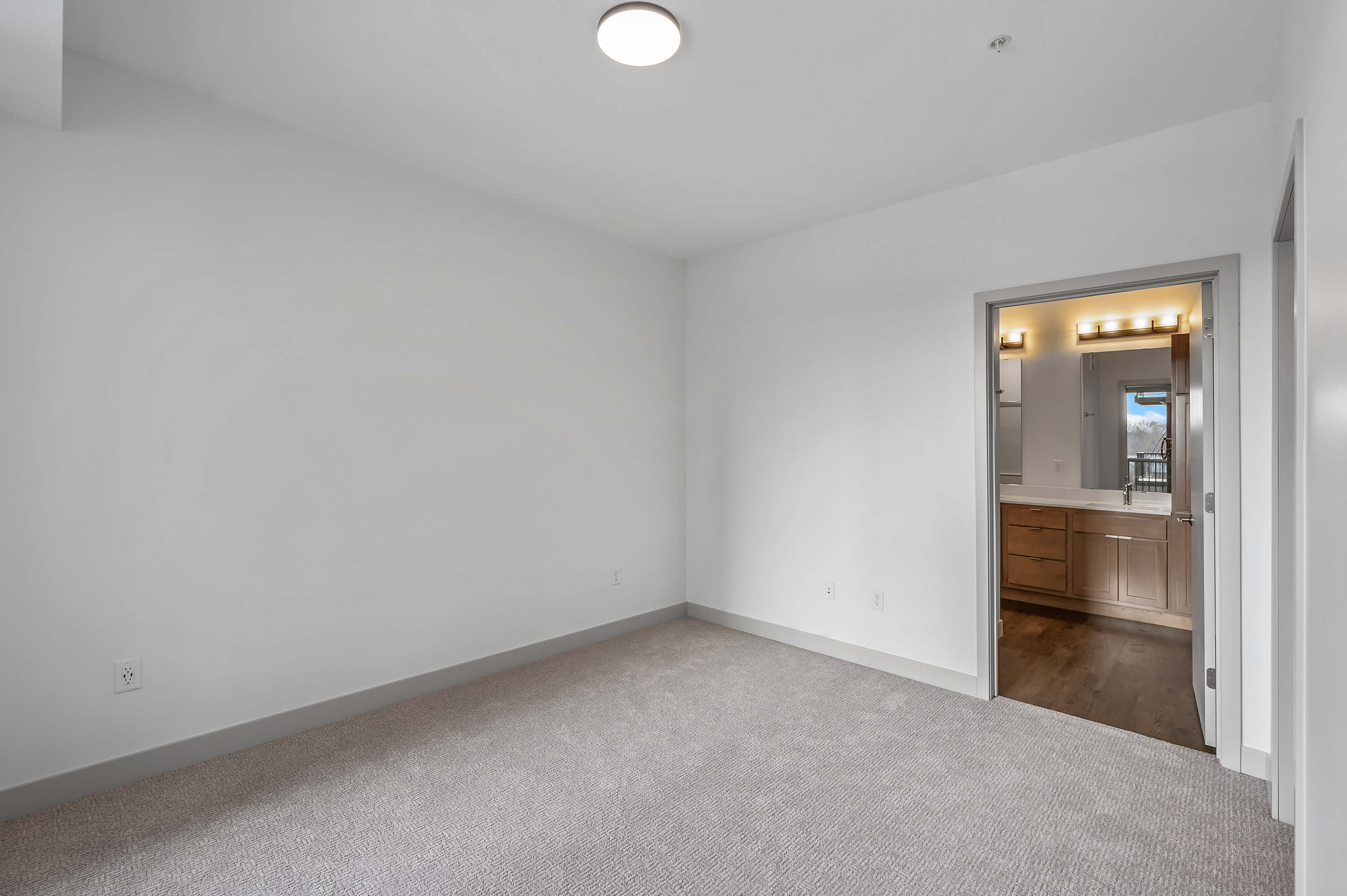 View of the living room area with a large window showcasing an outdoor scene and wooden floors.