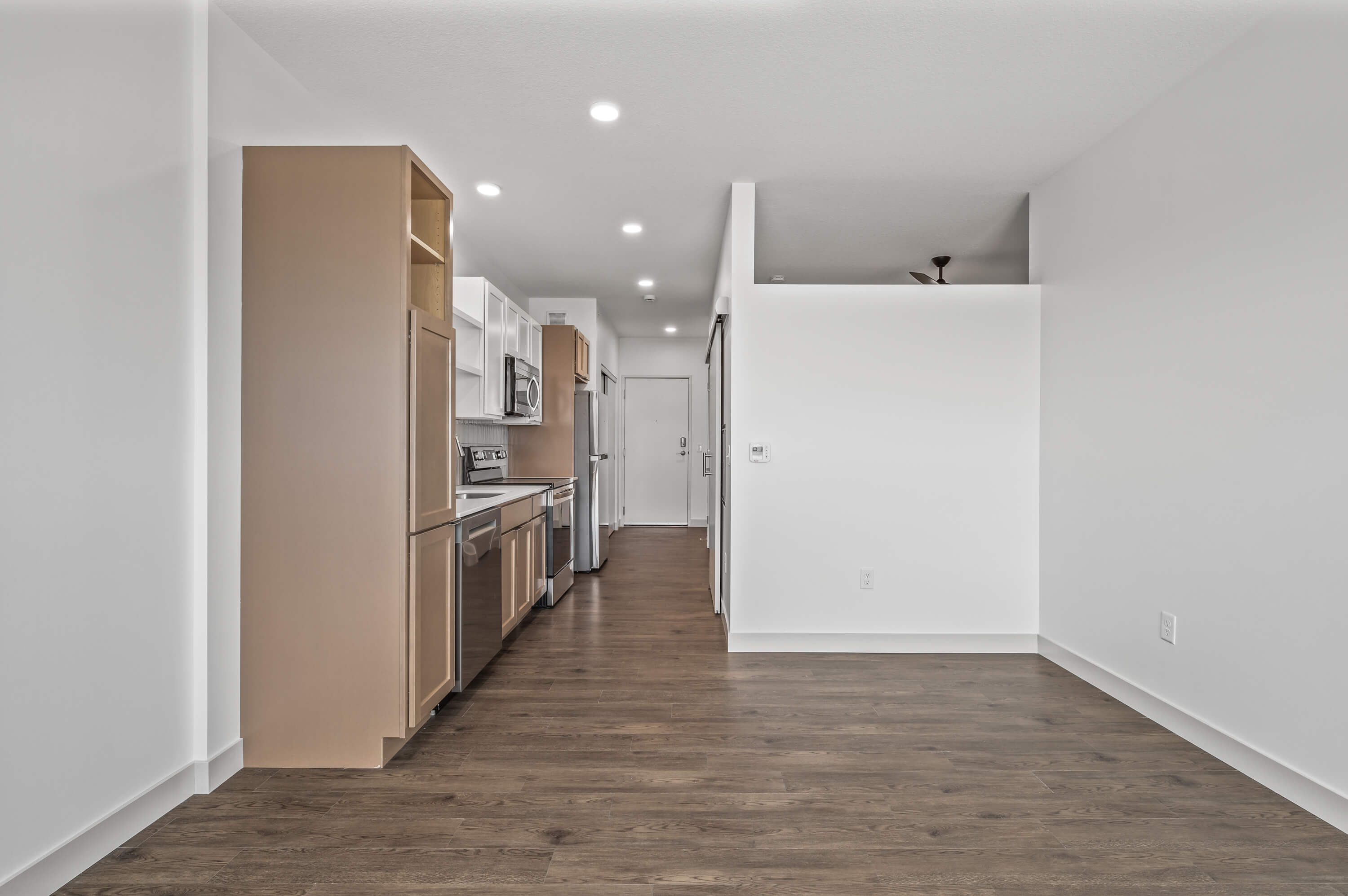 Open-concept kitchen and living area featuring white and beige cabinetry, stainless steel appliances, and wood flooring.