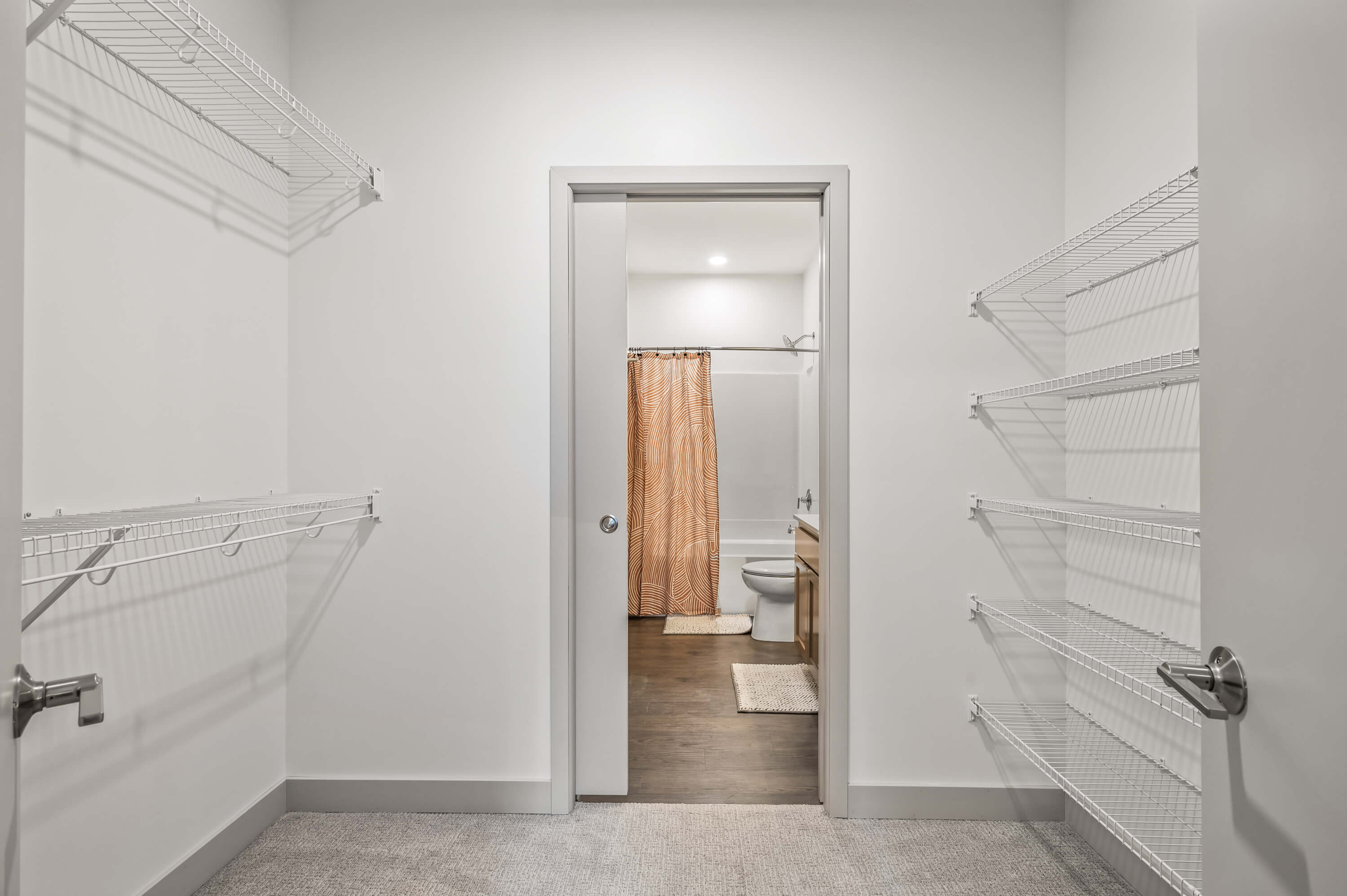 Spacious walk-in closet with wire shelving and a door leading to a bathroom with a patterned shower curtain.