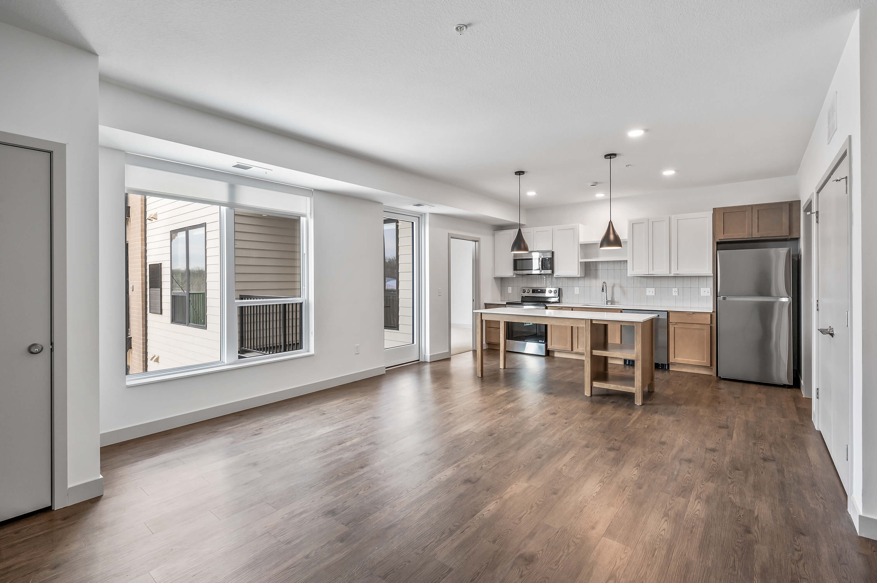 Spacious open-plan kitchen and living area featuring wood flooring, large windows, and modern lighting.