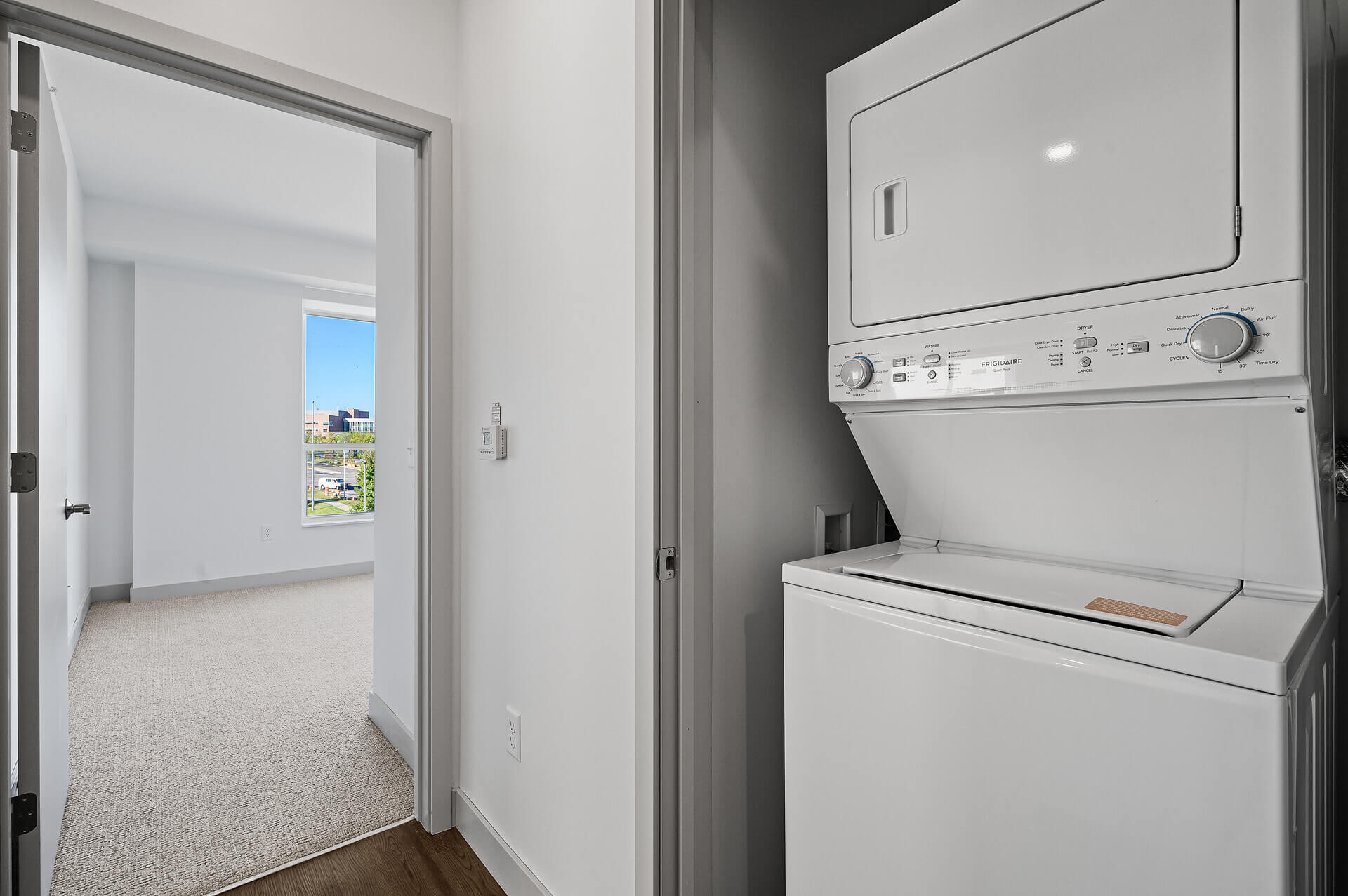 Stacked washer and dryer unit located in a hallway closet next to a bedroom.