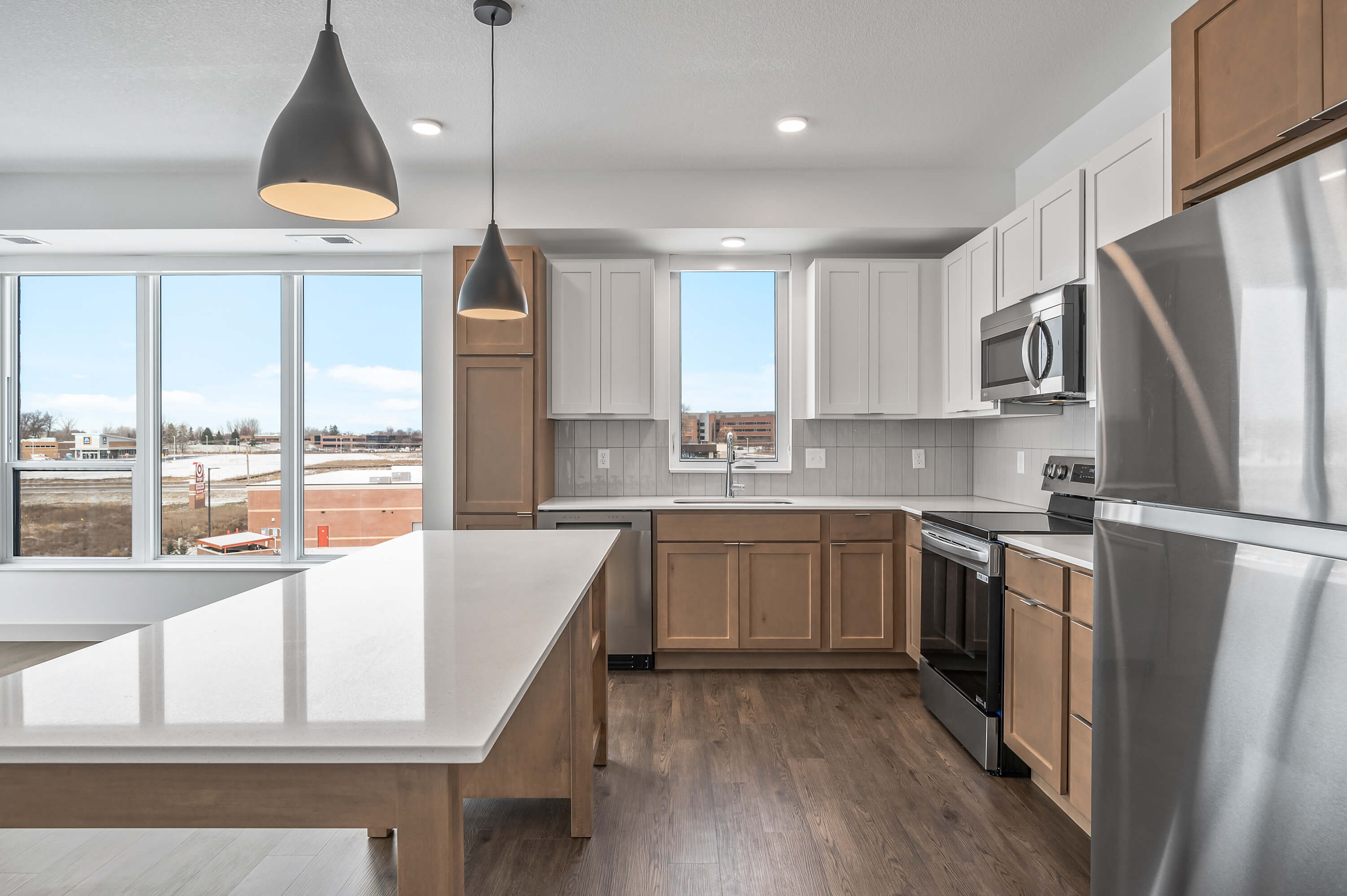 A close-up of the kitchen area featuring a central island, wooden cabinetry, stainless steel appliances, and tile backsplash.