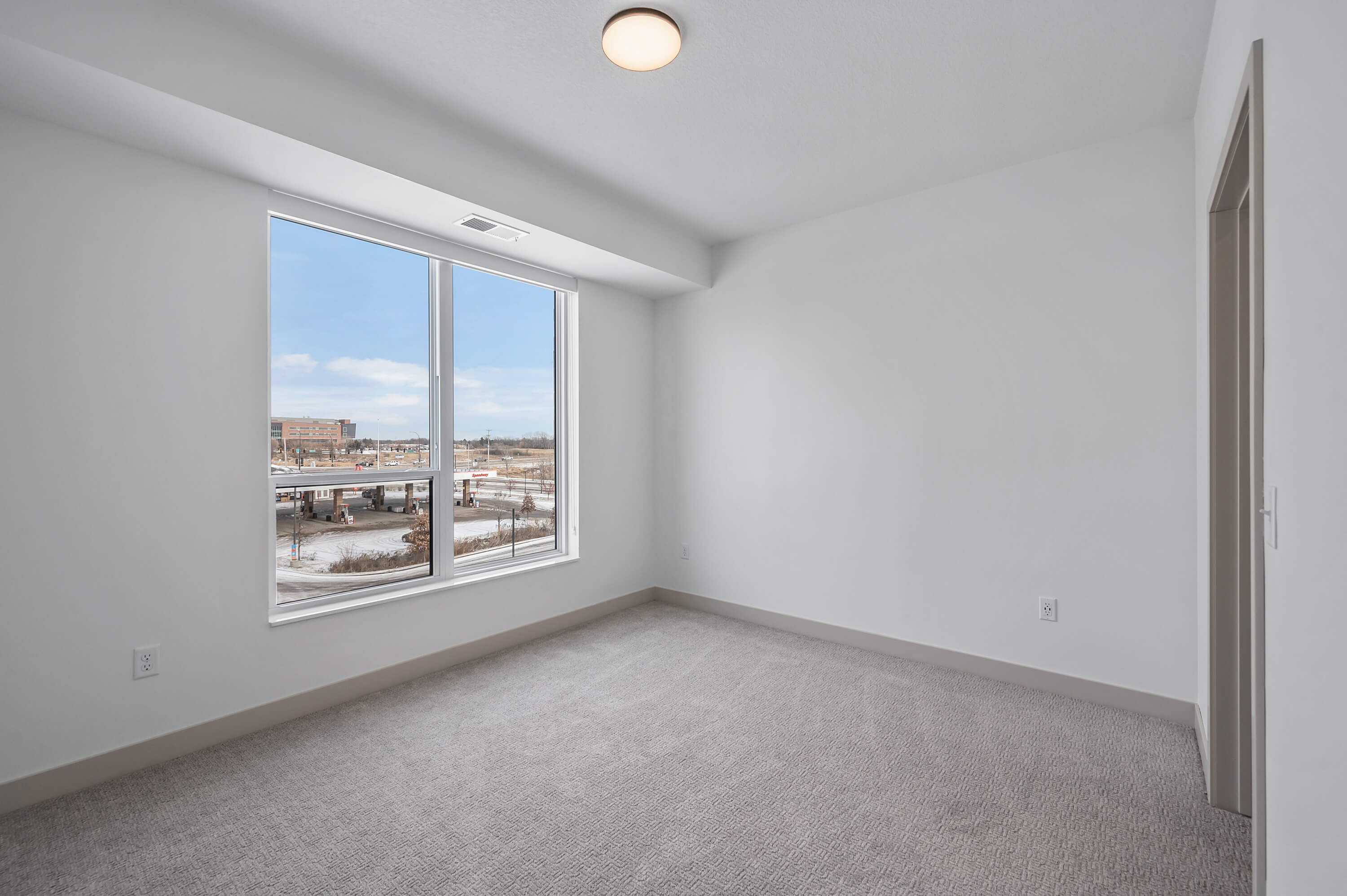 A bedroom with large windows, carpet flooring, and a view of the outdoors.