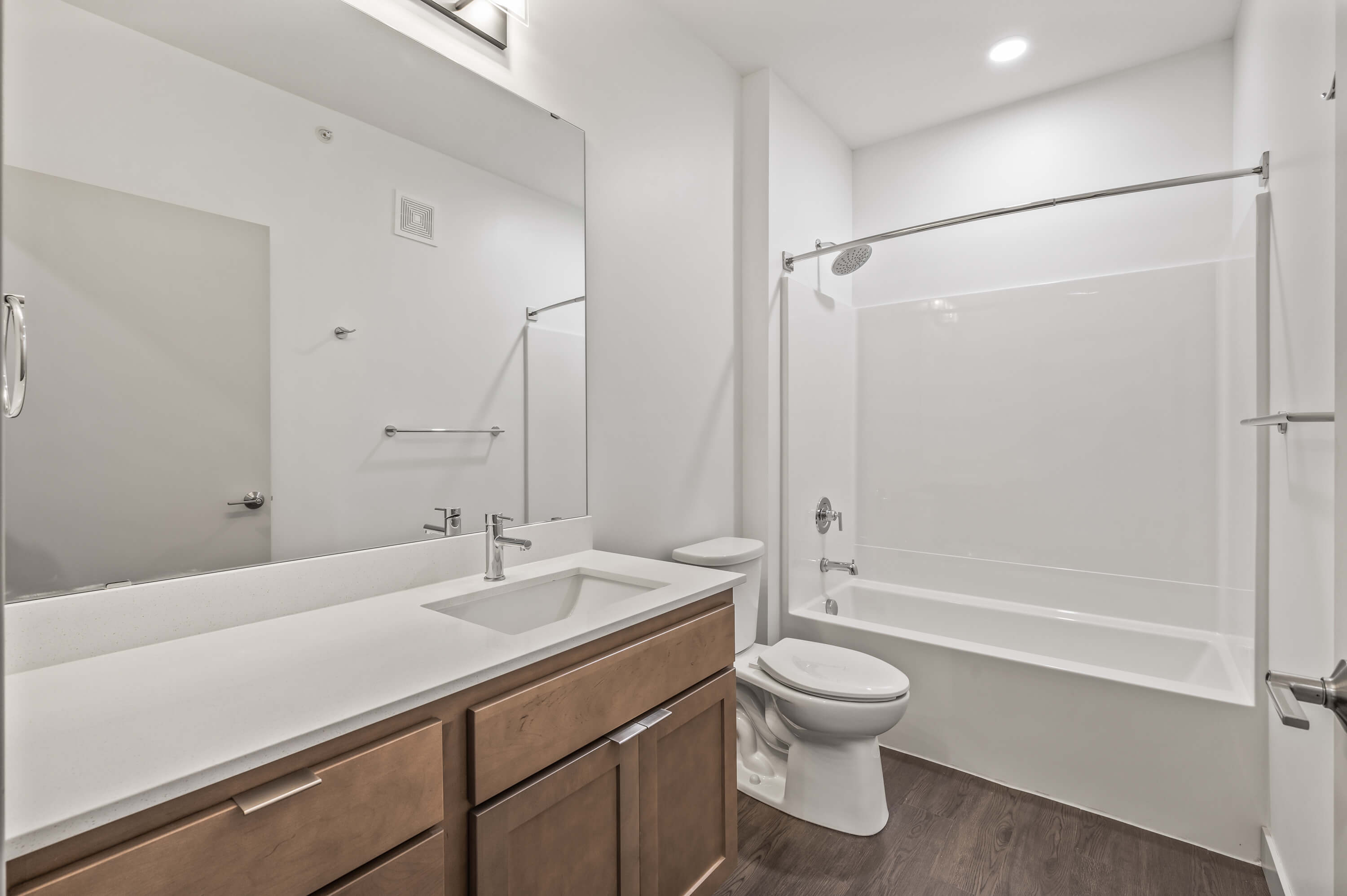 Bathroom featuring a large mirror, white countertop, light brown cabinets, and a shower-tub combo.