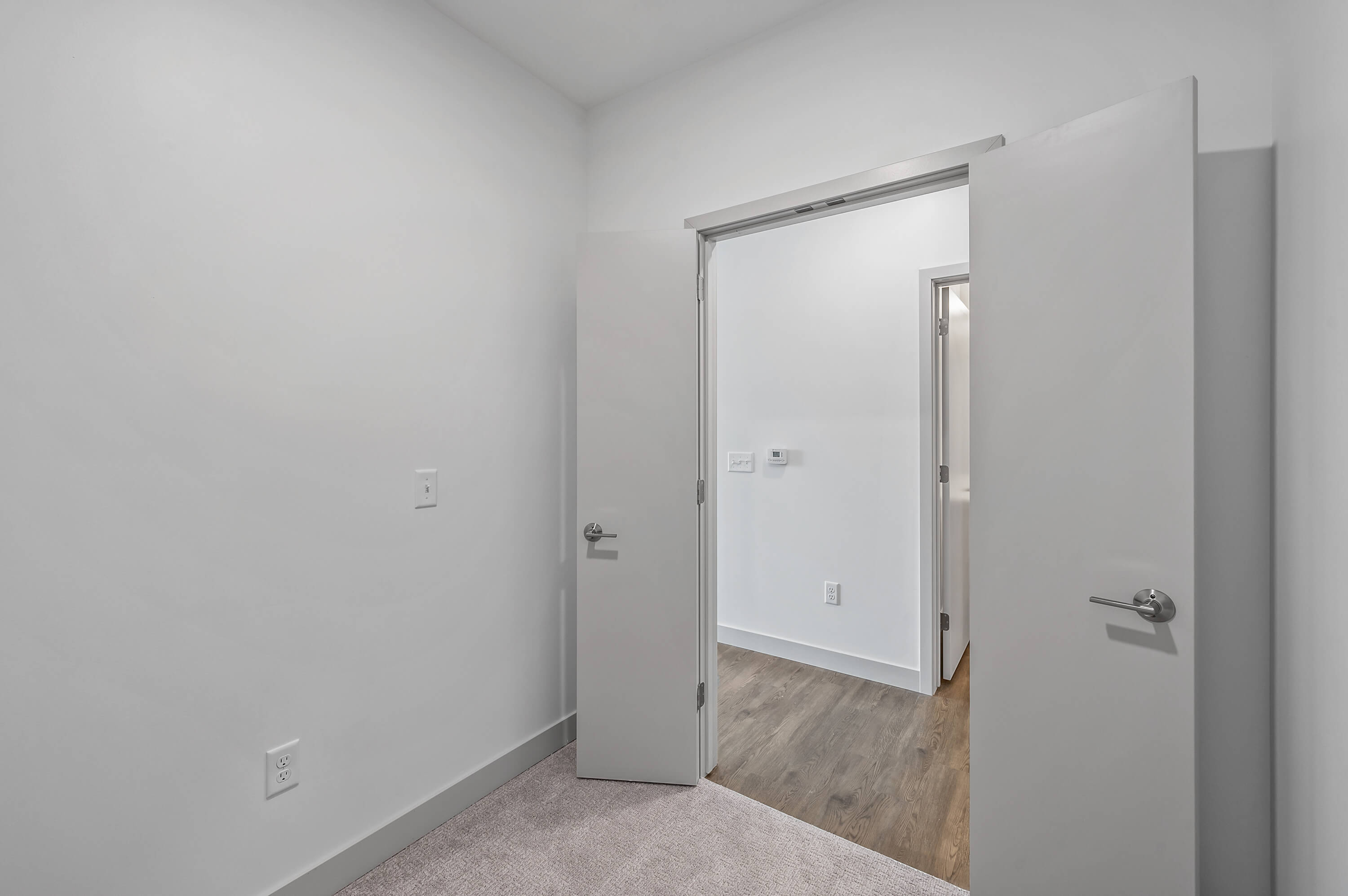 Room with double doors opening into a hallway, featuring carpet flooring and white walls.