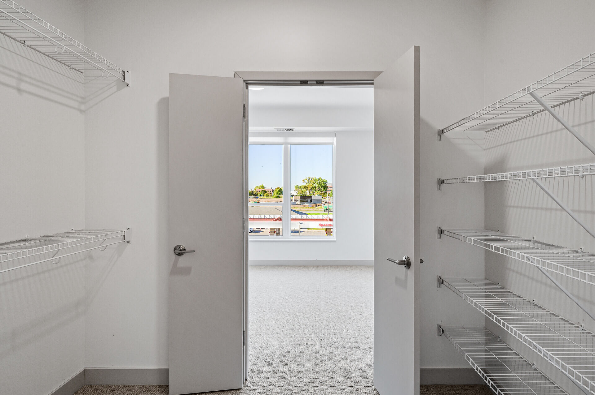 Walk-in closet with open double doors leading to a bedroom with a large window.