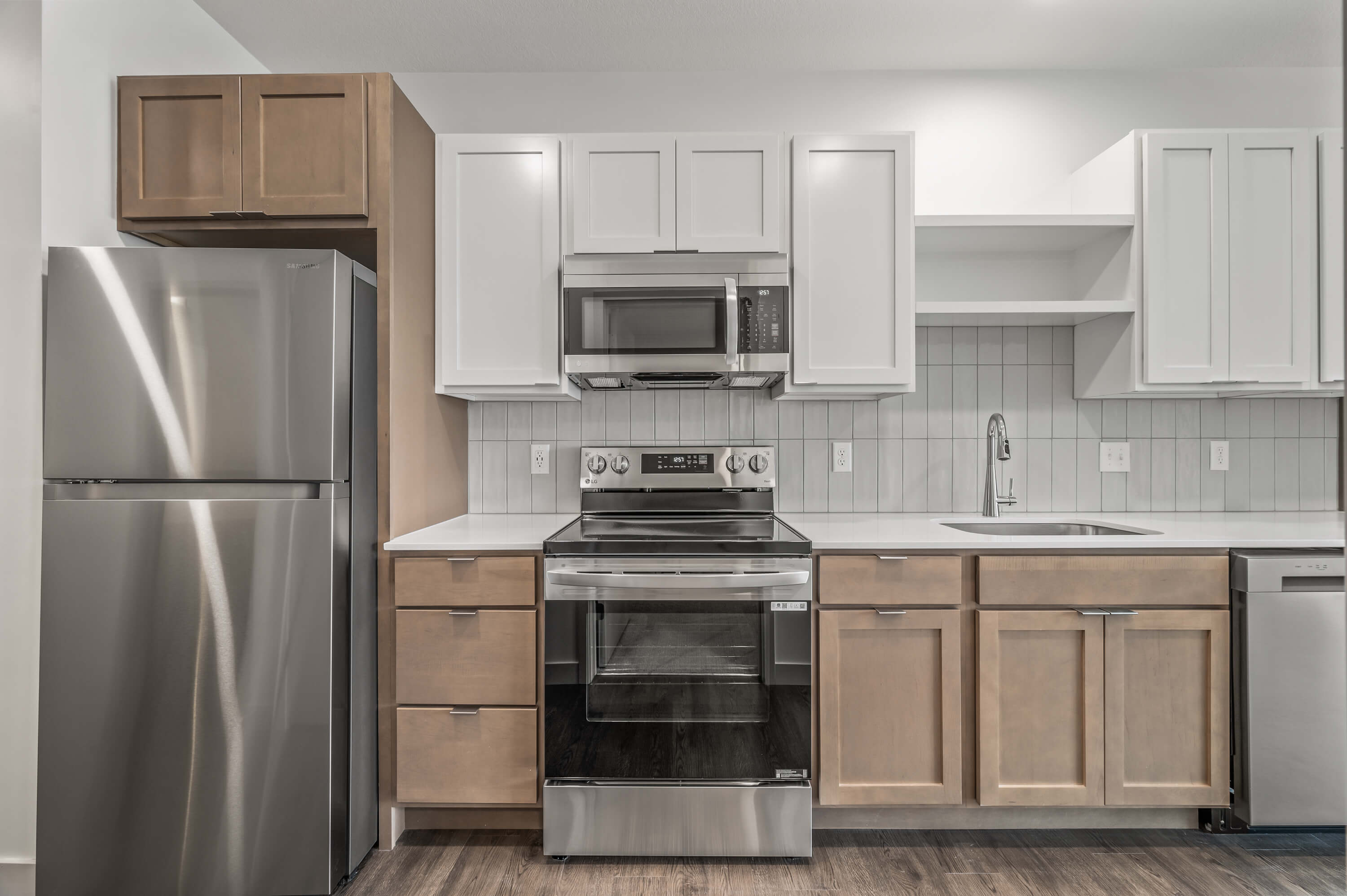 A close-up of a modern kitchen with stainless steel appliances, a tiled backsplash, and wooden cabinetry.