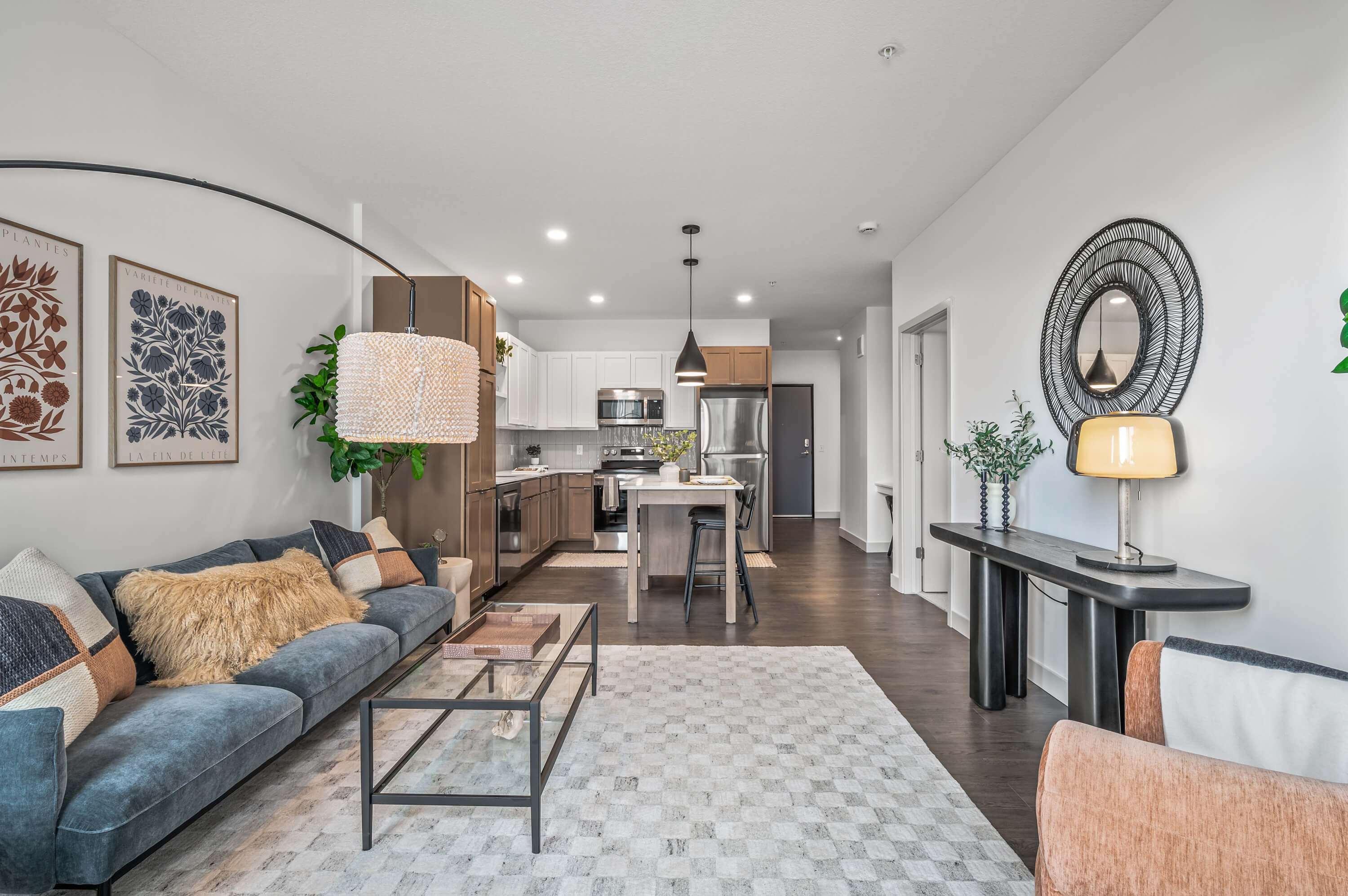 Contemporary living room with a stylish sofa, glass coffee table, and modern decor, adjacent to an open kitchen with wood and white cabinetry.