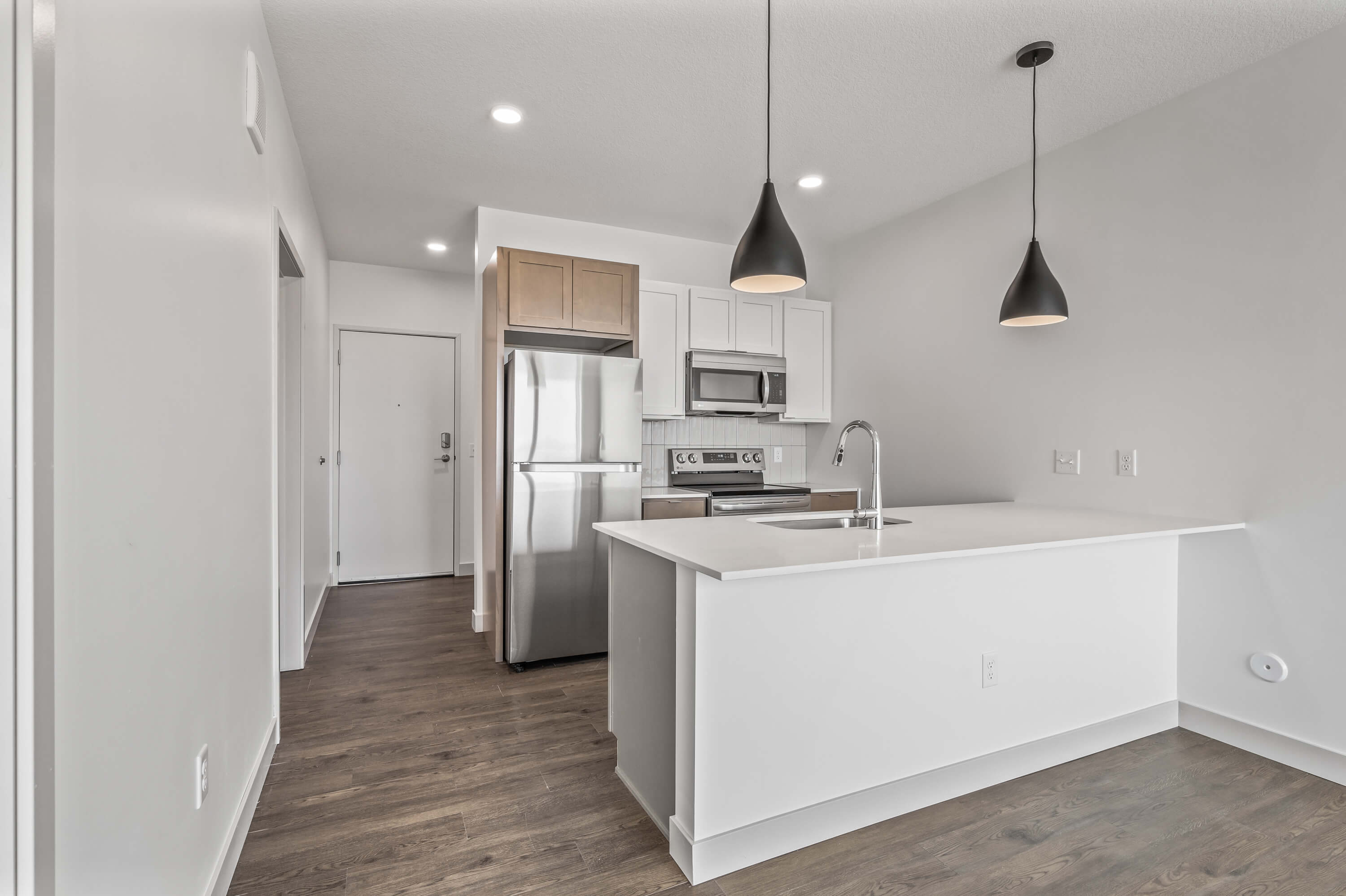 Kitchen and island with stainless steel appliances, pendant lights, and open shelving.