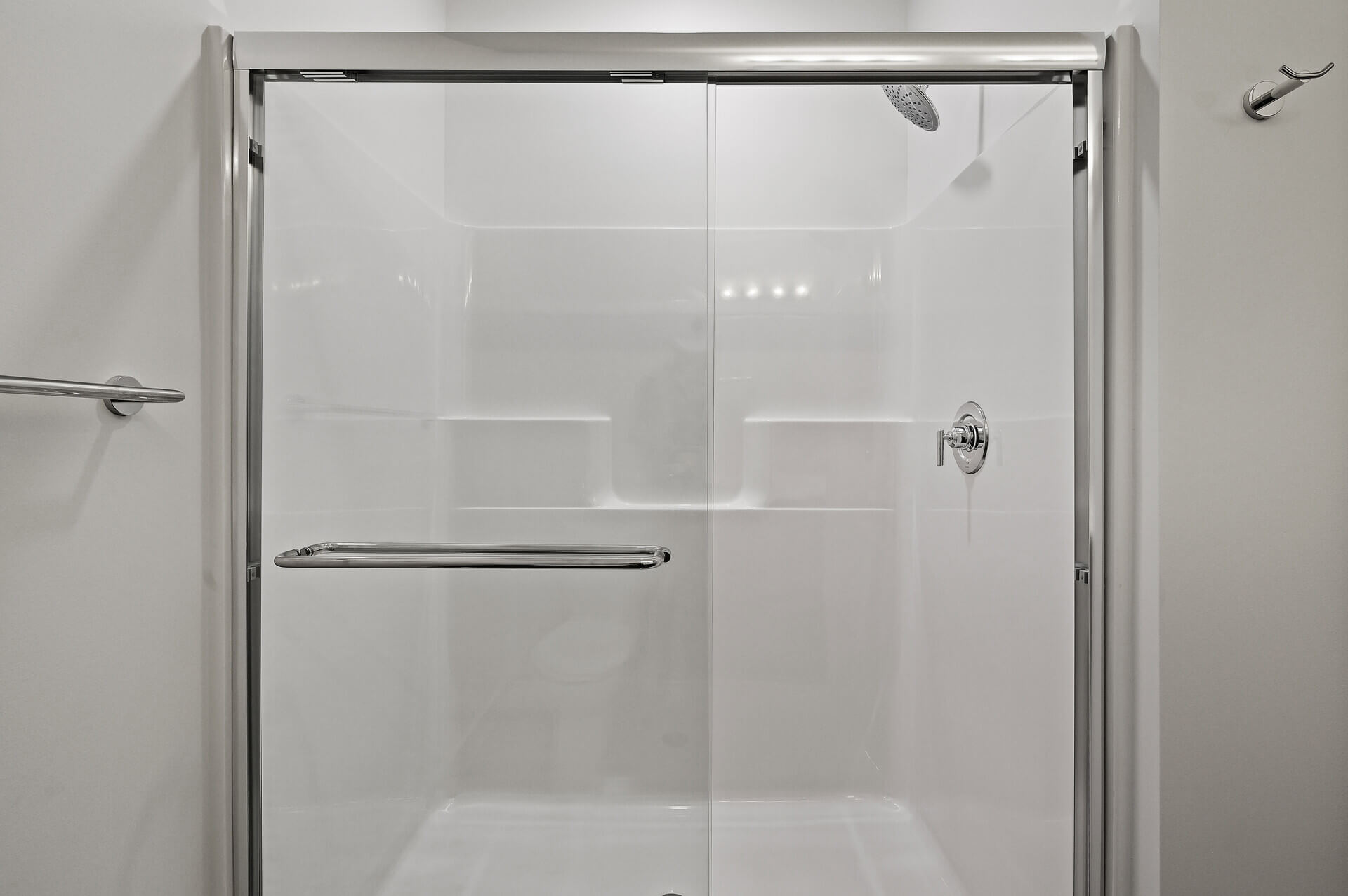 Glass-enclosed shower with chrome hardware and bright white tile.