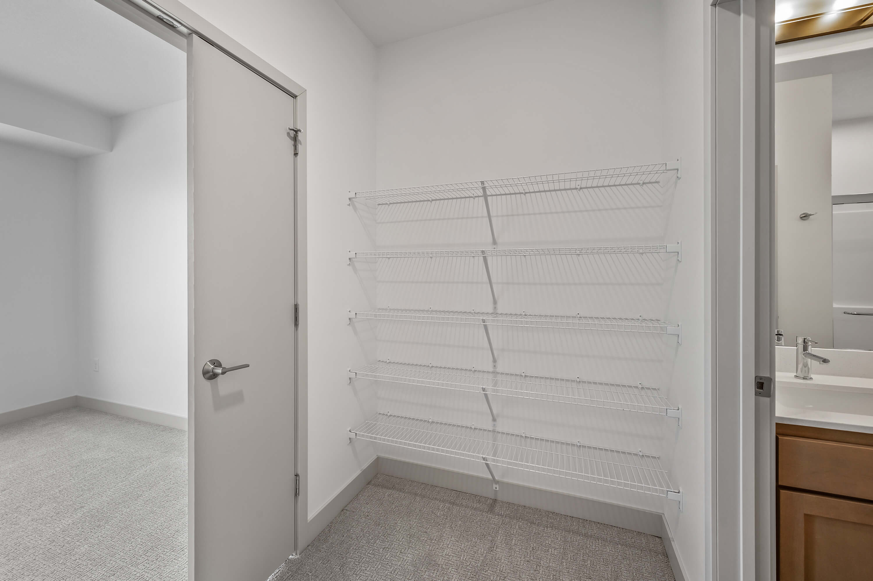 A walk-in closet with white wire shelving, located next to a bathroom.