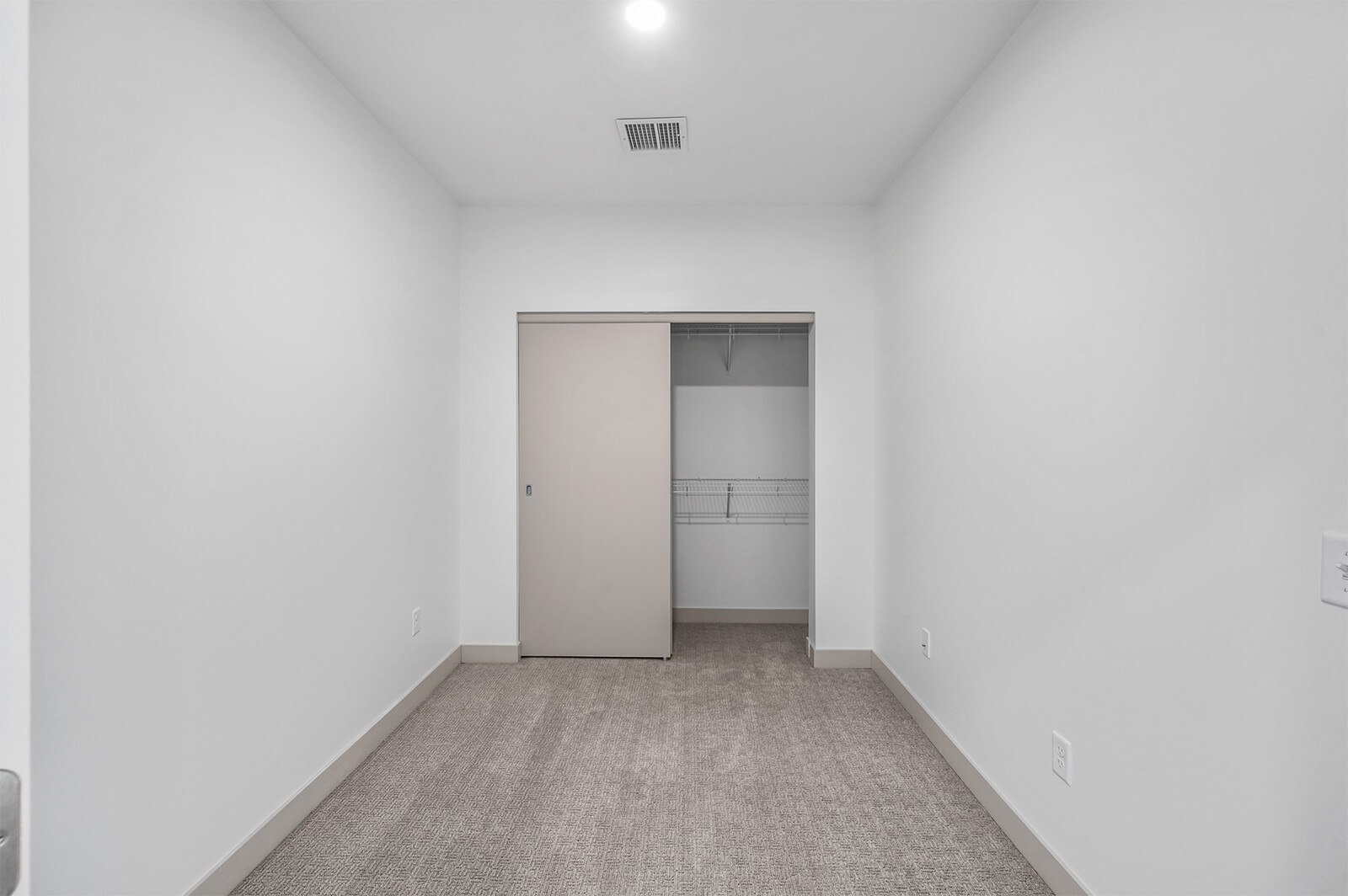 Carpeted room with sliding closet doors open to reveal shelving