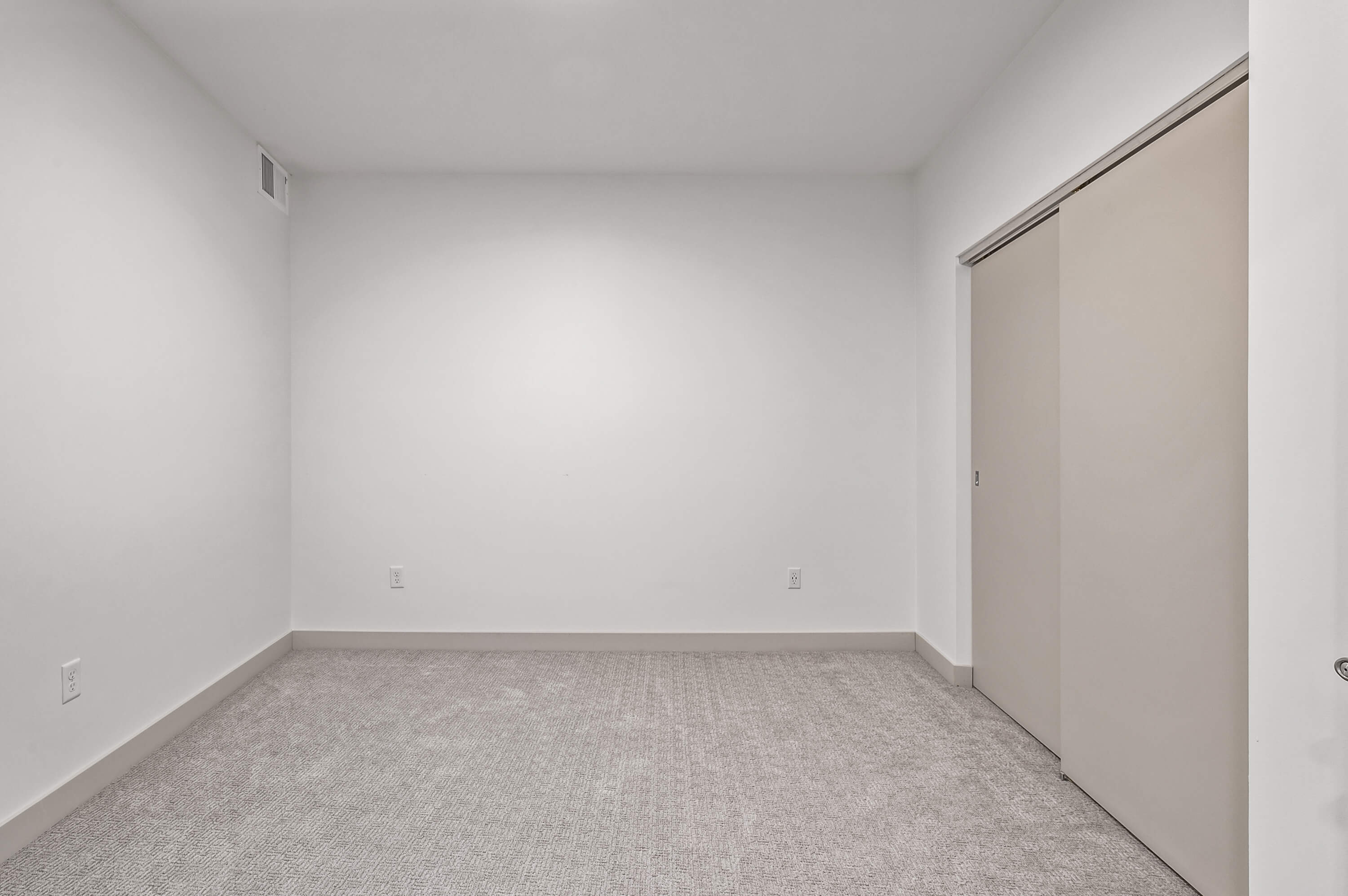 A similar room with beige carpet, white walls, and a window but from a slightly different perspective.