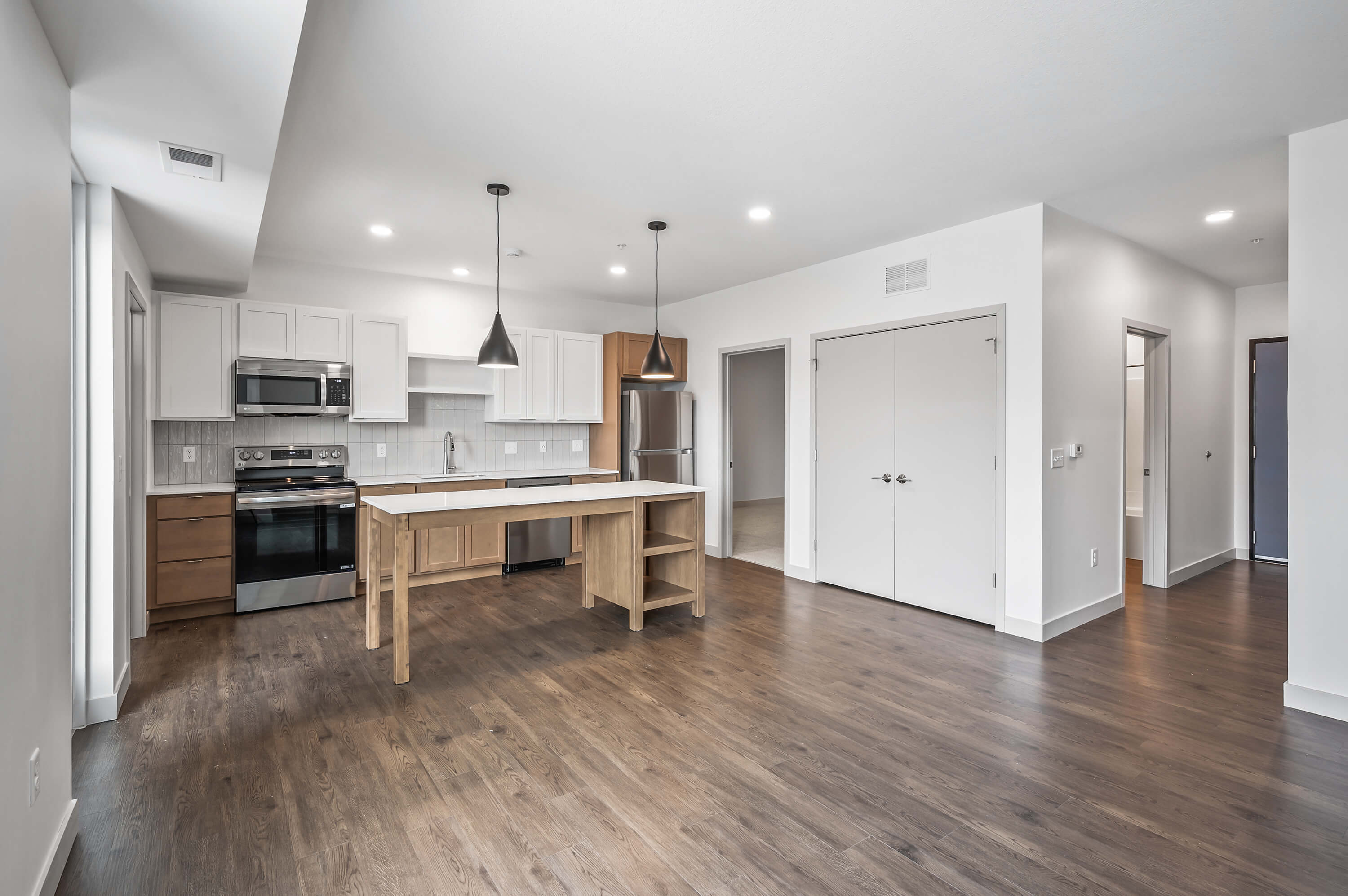 Modern kitchen with white and wood cabinetry, pendant lights, and stainless steel appliances.