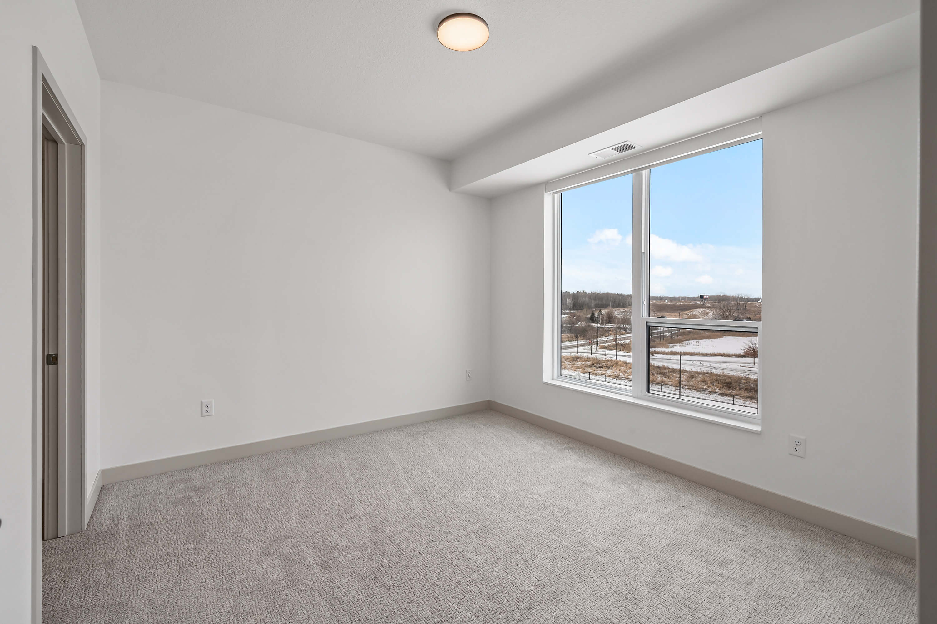 A second bedroom with large windows, carpet flooring, and a scenic outdoor view.