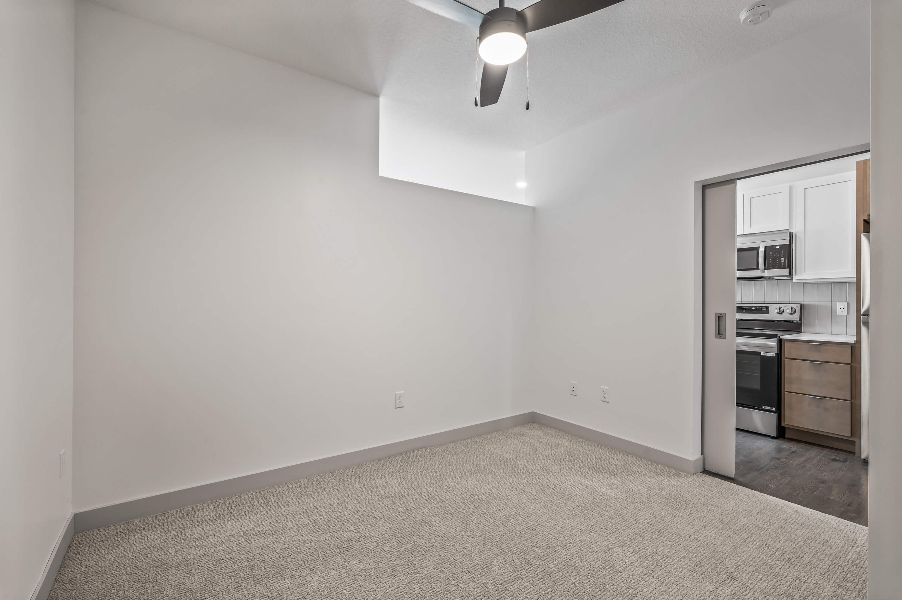 Another angle of the bedroom showing white walls, gray carpet, a ceiling fan, and a sliding closet door.