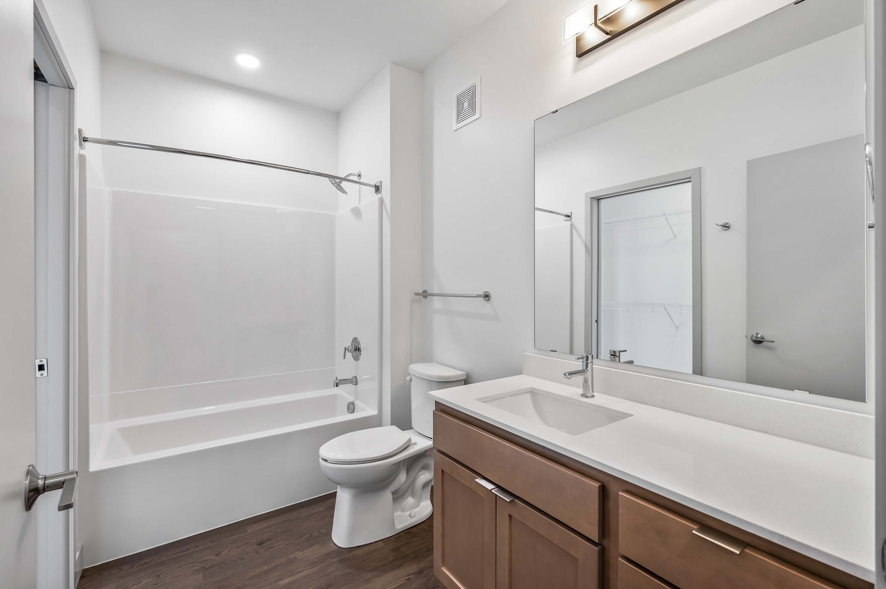 A bathroom with a single vanity, bathtub with a shower, and white walls, complemented by wooden cabinetry.