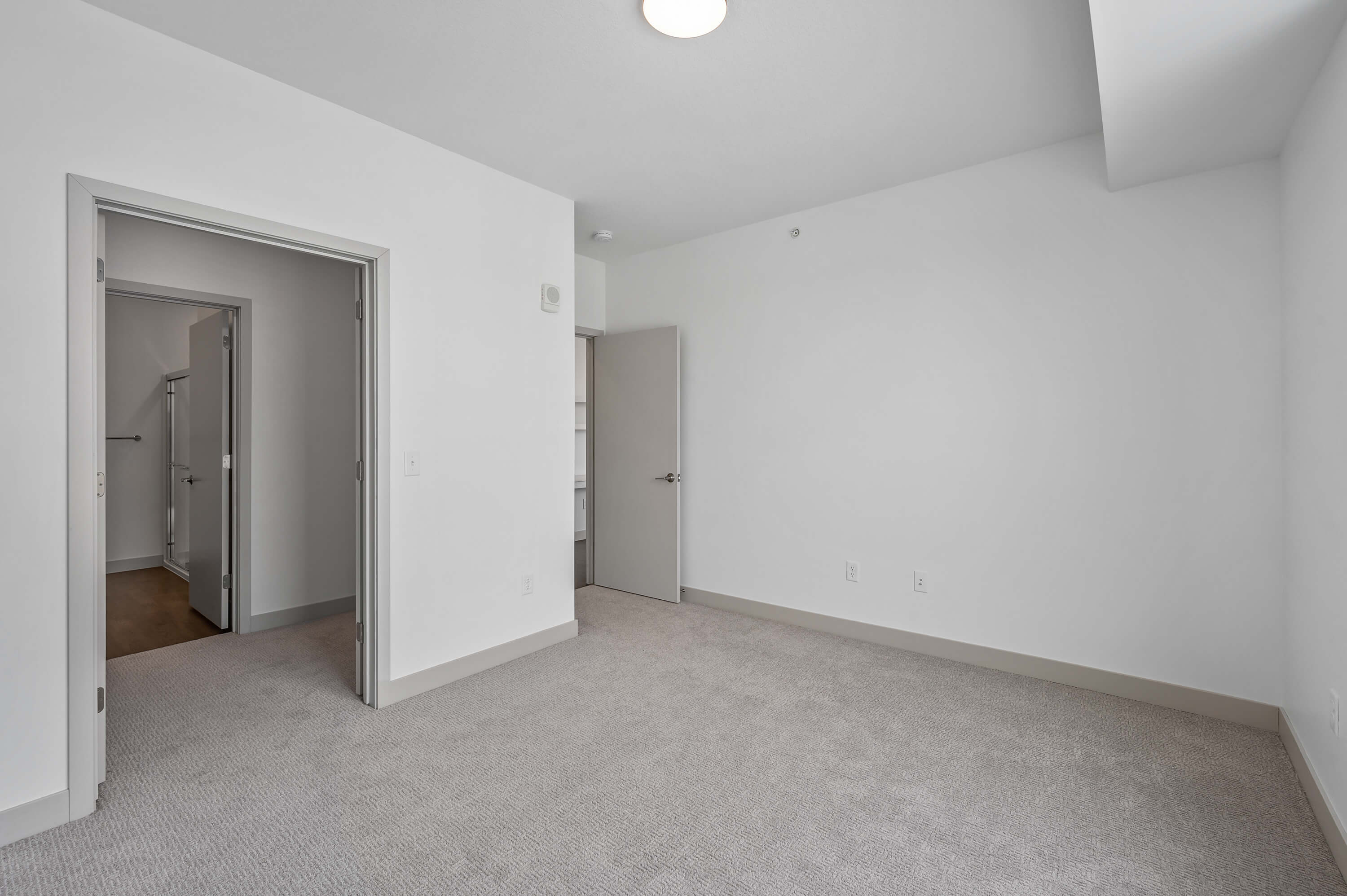 A bedroom with neutral carpet, a doorway leading to a bathroom, and an additional door to a closet.