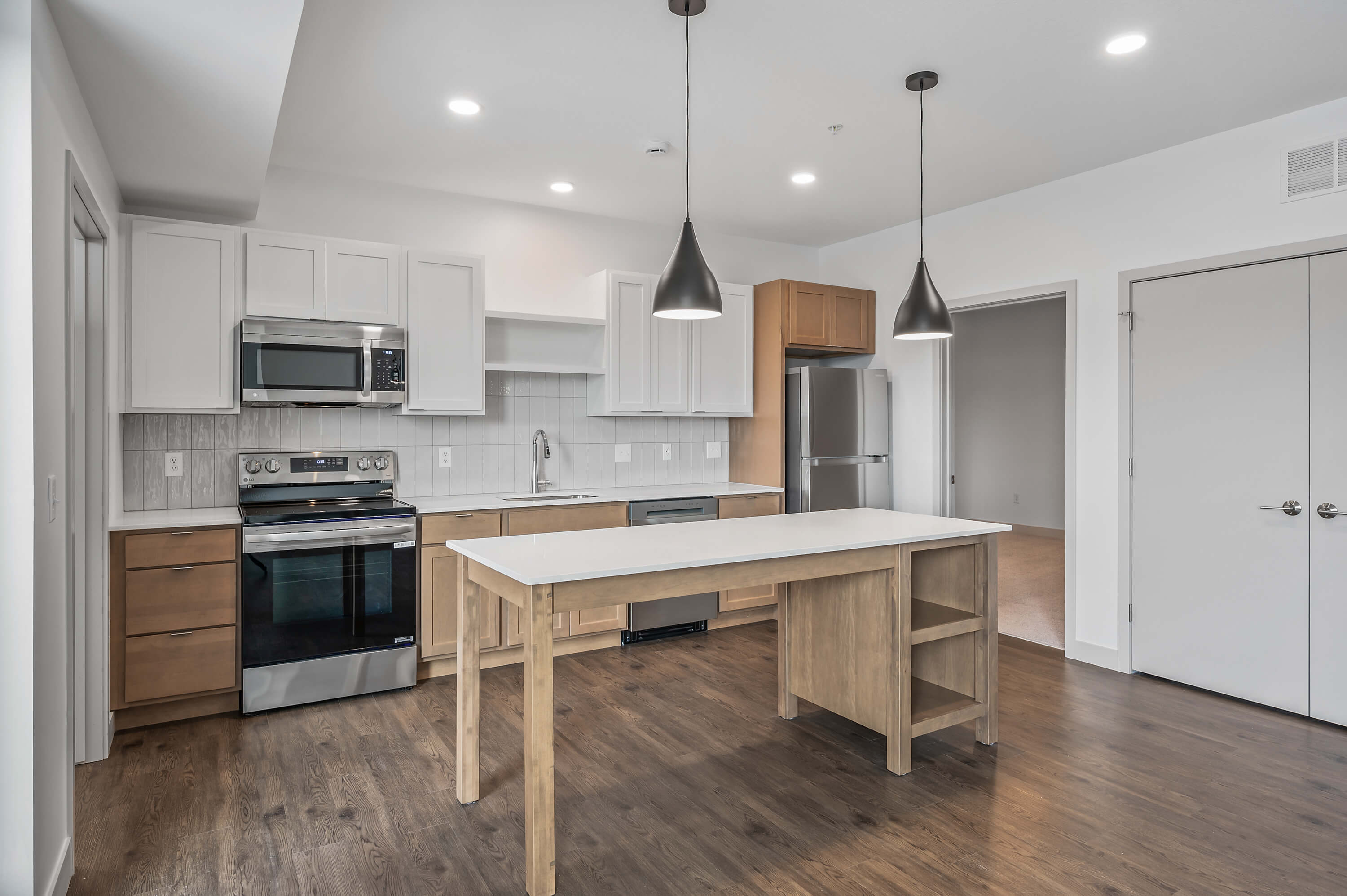 Modern kitchen and living space with a large countertop, pendant lights, and wood flooring.