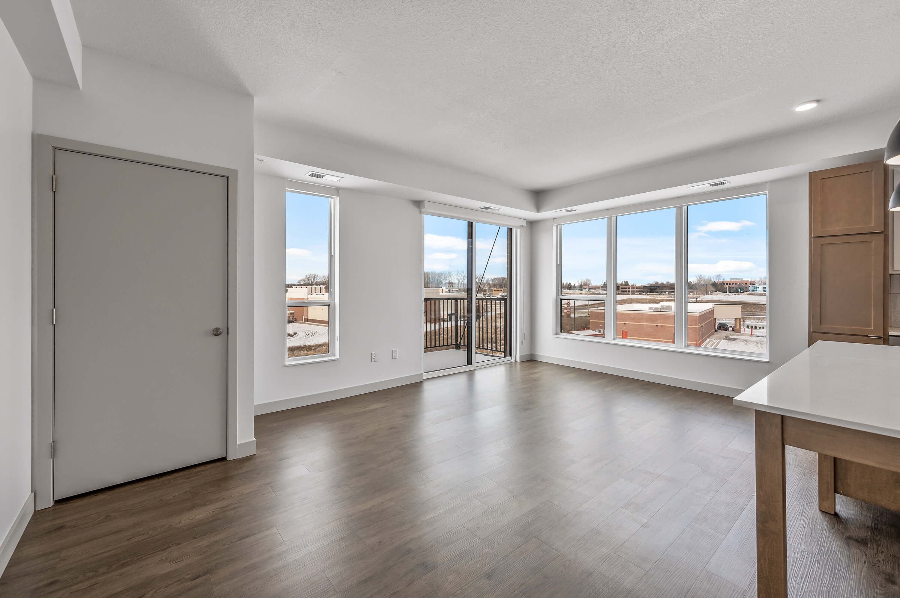 A bright living space featuring large windows and a balcony door, showcasing an outdoor view with a modern wood floor.