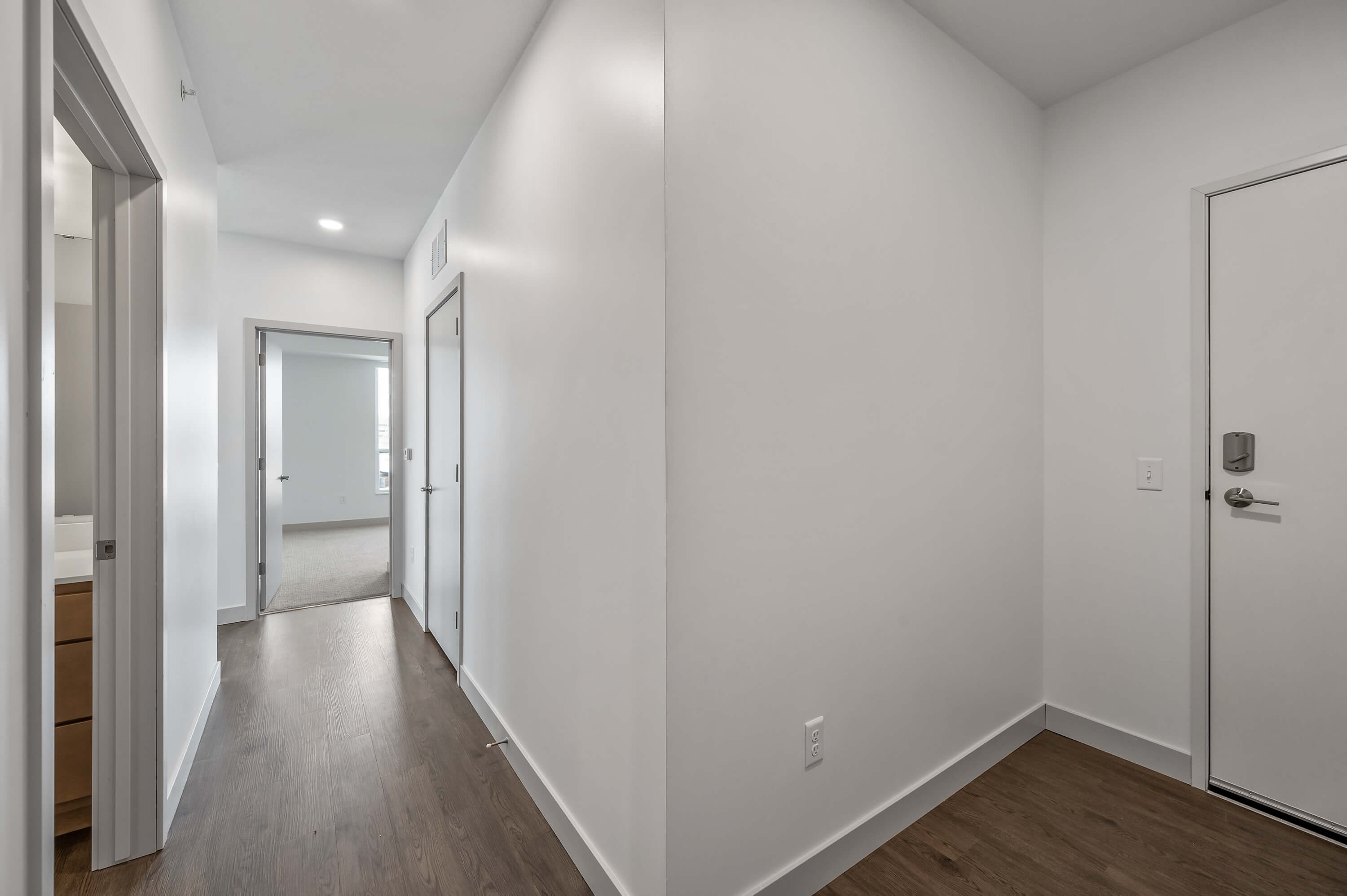 A hallway with a white interior and wood flooring, featuring doors leading to different rooms.