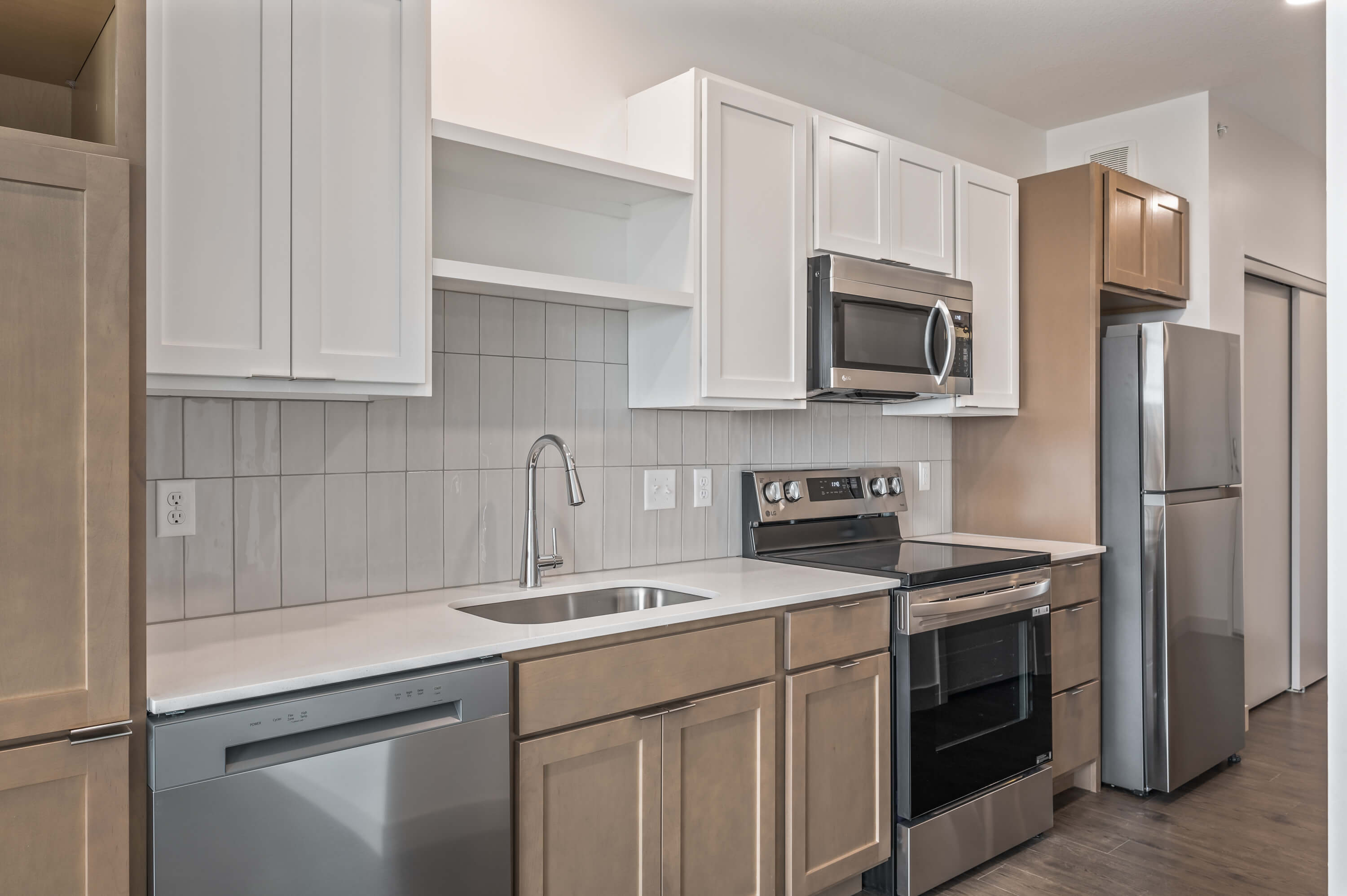 Close-up view of a contemporary kitchen showcasing white upper cabinets, light brown lower cabinets, a tile backsplash, and stainless steel appliances.