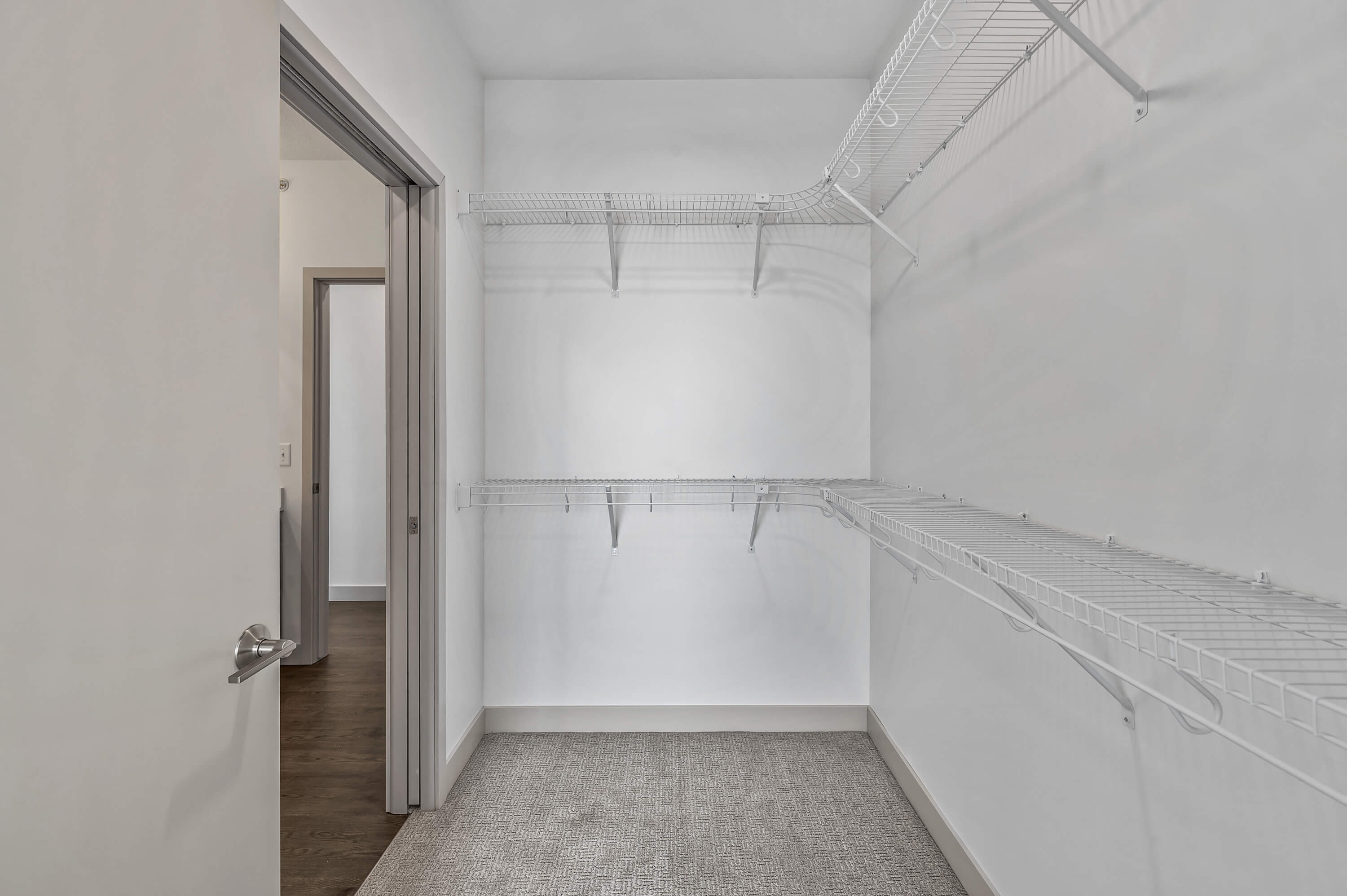 A spacious walk-in closet with white wire shelving on multiple walls, adjacent to the bedroom.