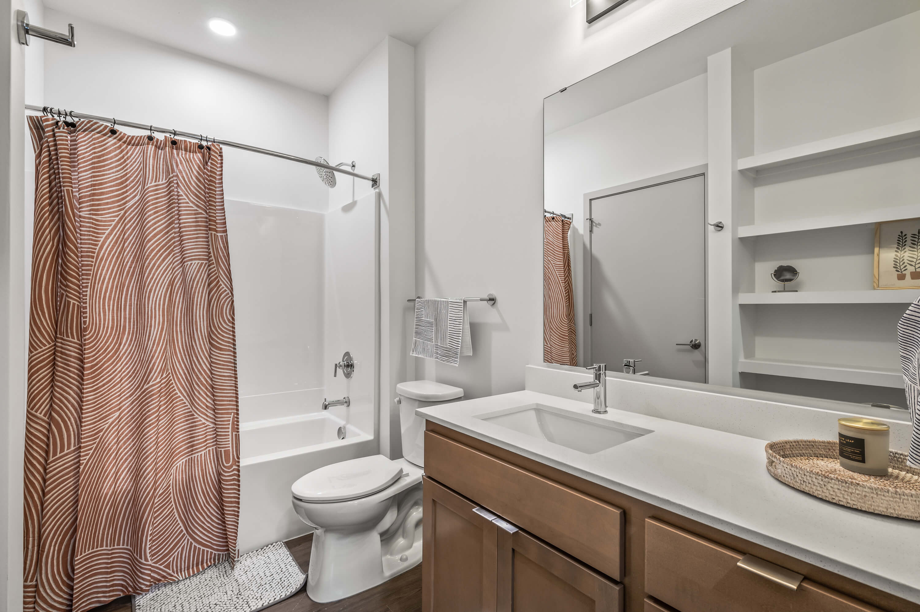 Contemporary bathroom with wooden vanity, sleek countertop, and a patterned shower curtain.